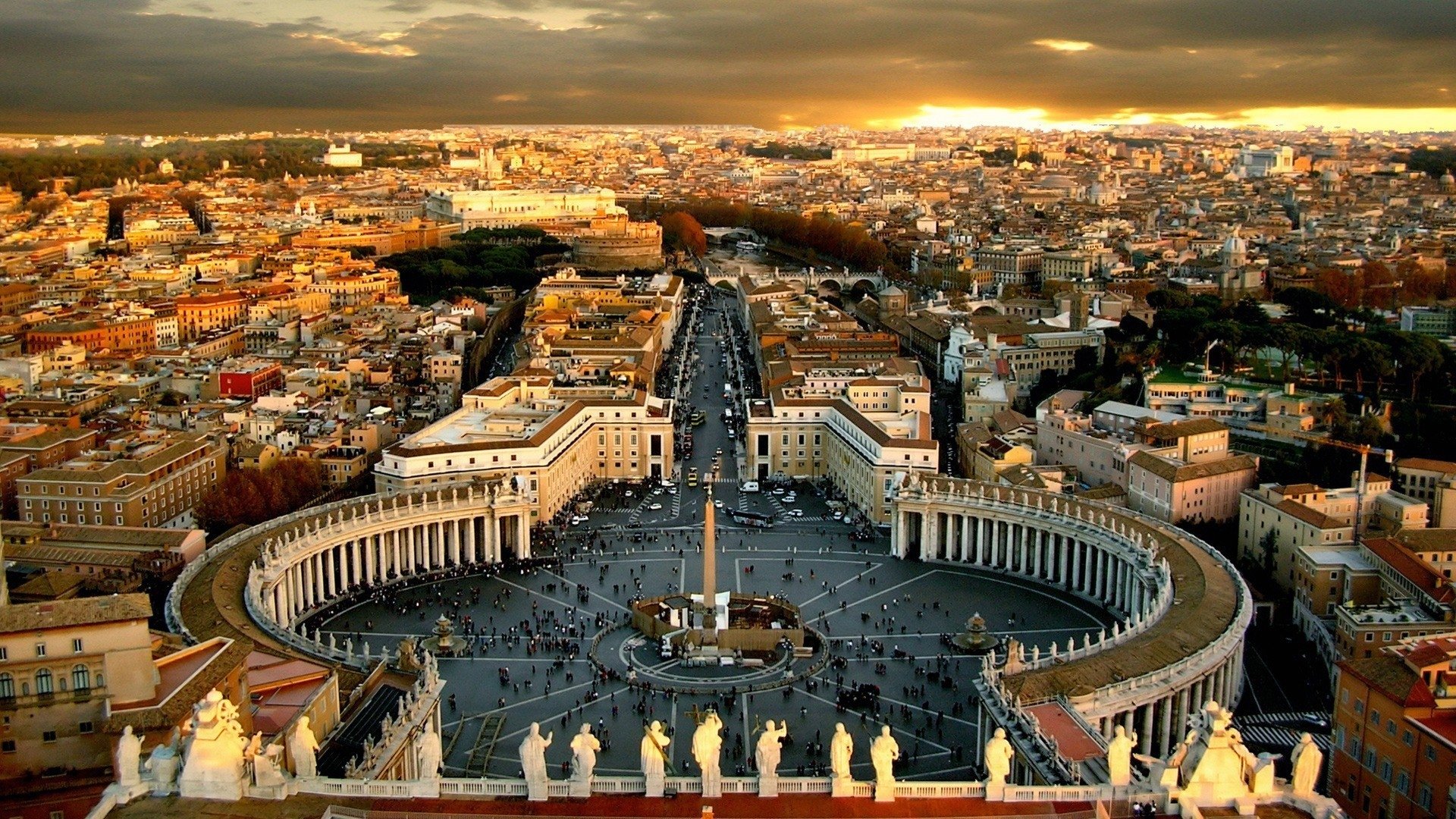 A panoramic view of St. Peter's Square in Vatican City, with religious statues and surrounding buildings glowing under a sunset sky in Rome.