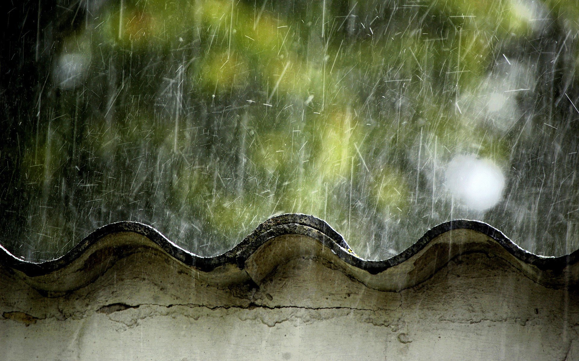 A close-up of raindrops cascading down a textured surface, with blurred greenery in the background, capturing the essence of a rainy day in photography.