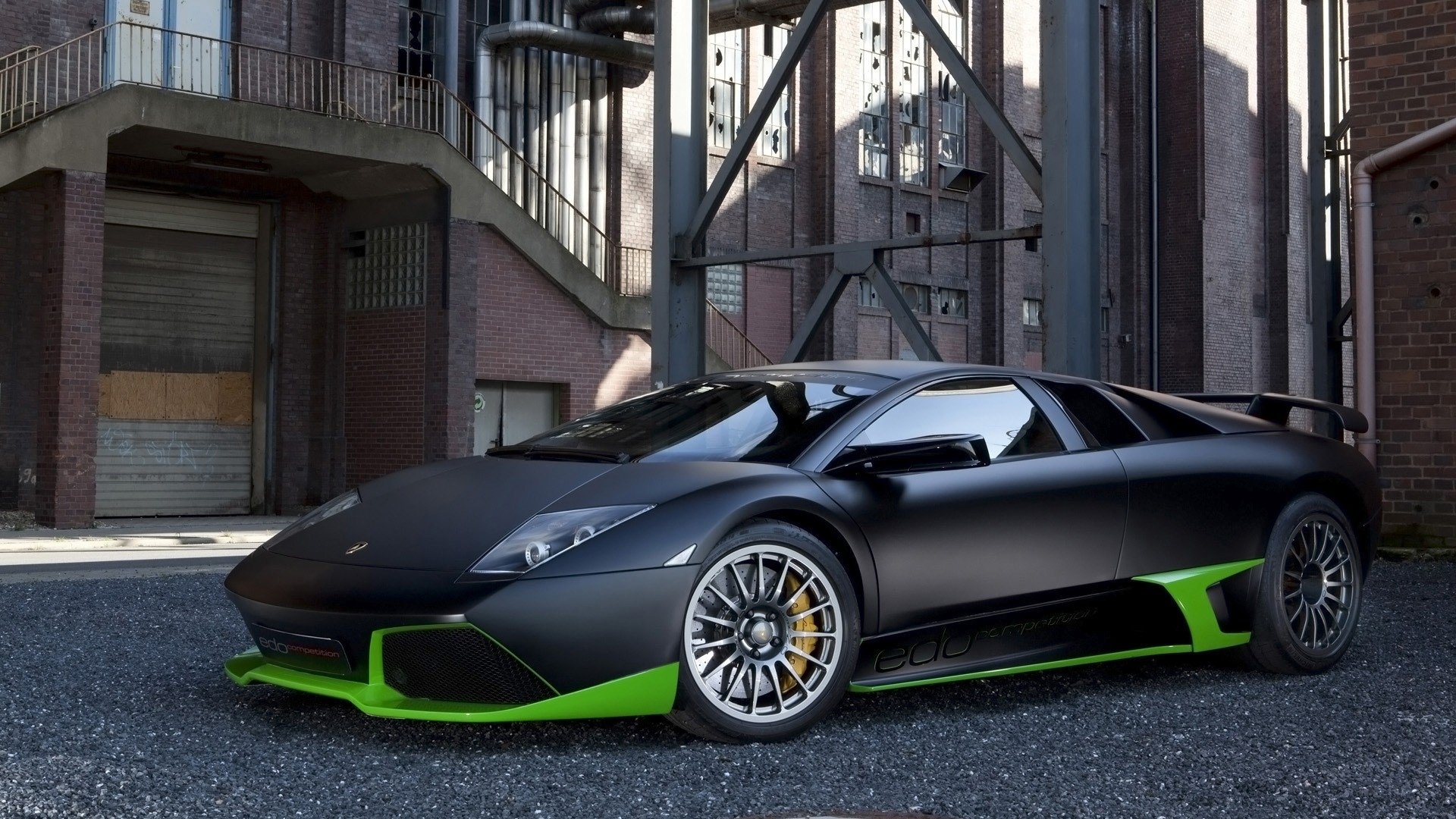 A sleek Lamborghini Murcielago is parked against an urban backdrop, showcasing its striking black and green design, emphasizing its sporty and powerful presence.