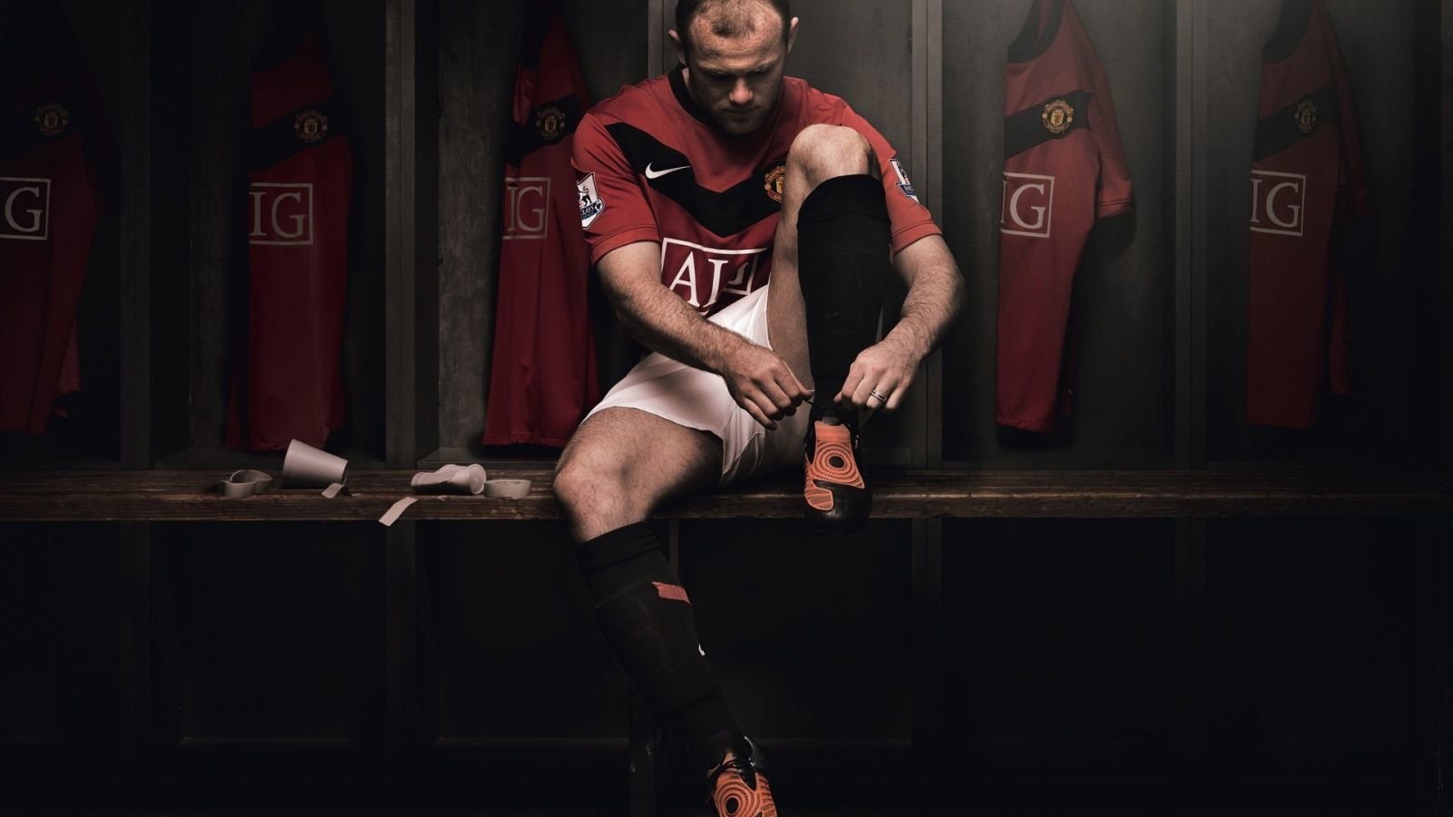 Wayne Rooney laces up his cleats in a dimly lit locker room, showcasing his dedication to sports and preparation for the game ahead.