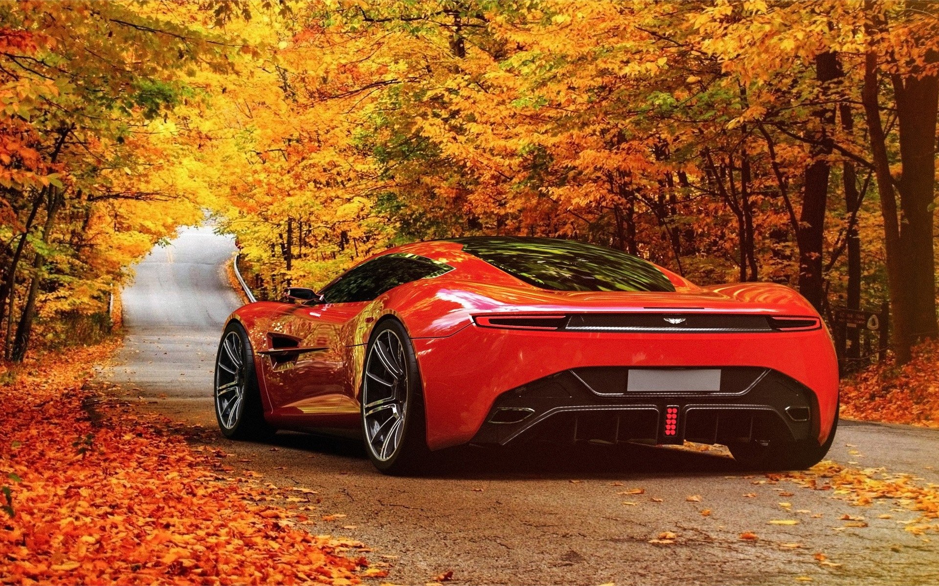 A sleek red Aston Martin vehicle parked on a leaf-covered road surrounded by vibrant autumn trees.