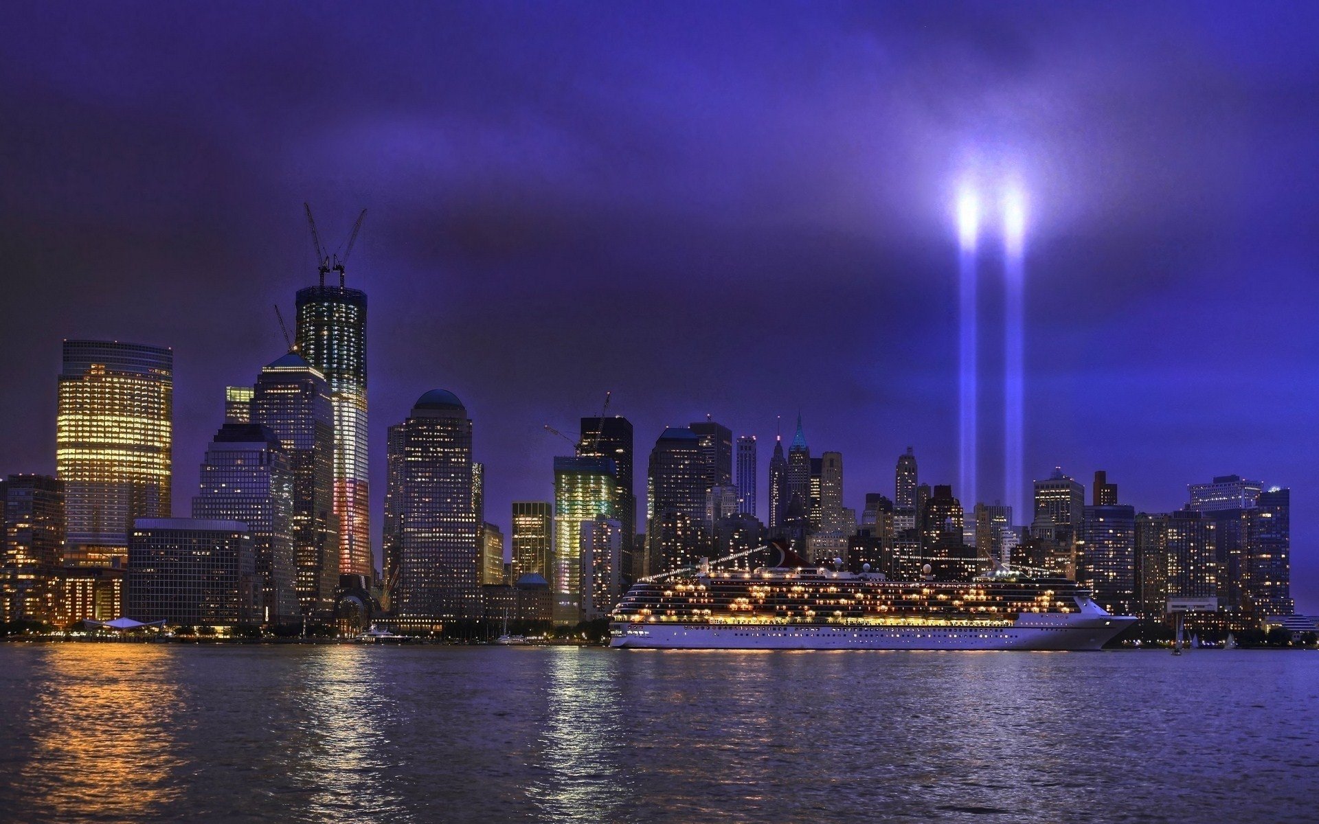A nighttime view of New York City, showcasing its skyline illuminated by twin beams of light against a moody sky, with a prominent ship docked nearby.
