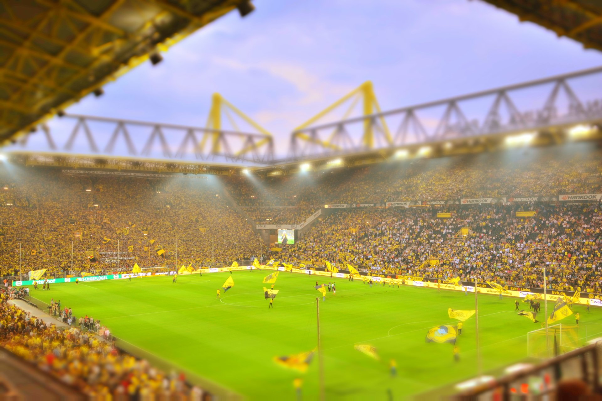 A vibrant scene at a Borussia Dortmund football match in Germany, showcasing enthusiastic fans waving flags in a packed stadium under a colorful sky.