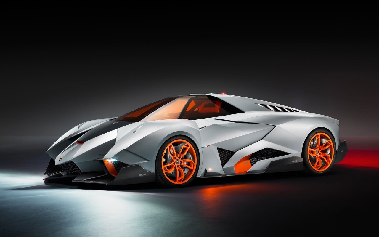 Sleek silver Lamborghini Egoista with sharp angular design and vibrant orange accents on wheels and interior, showcased against a dark background.