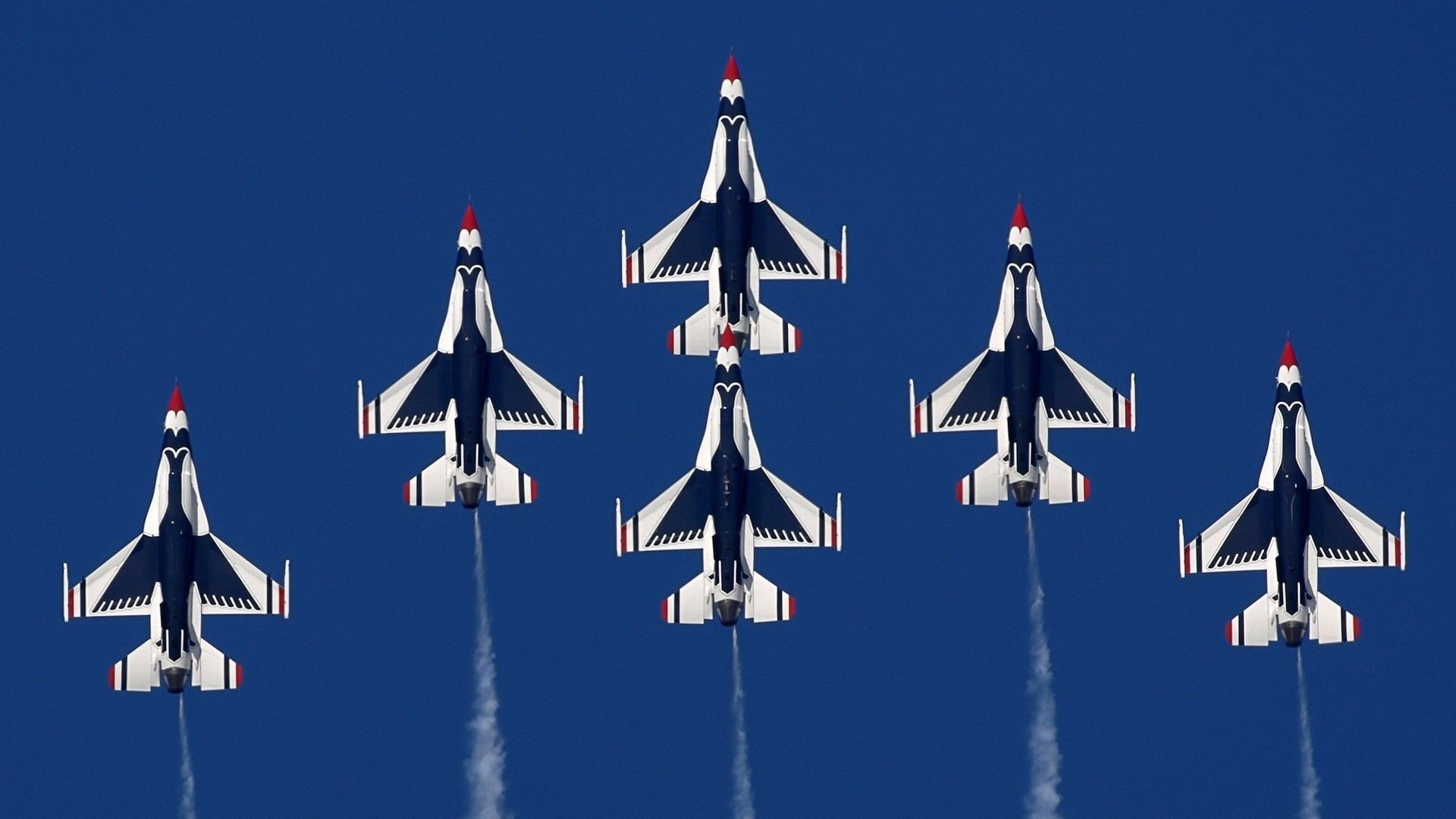 Six military jets fly in tight formation during an air show against a clear blue sky.