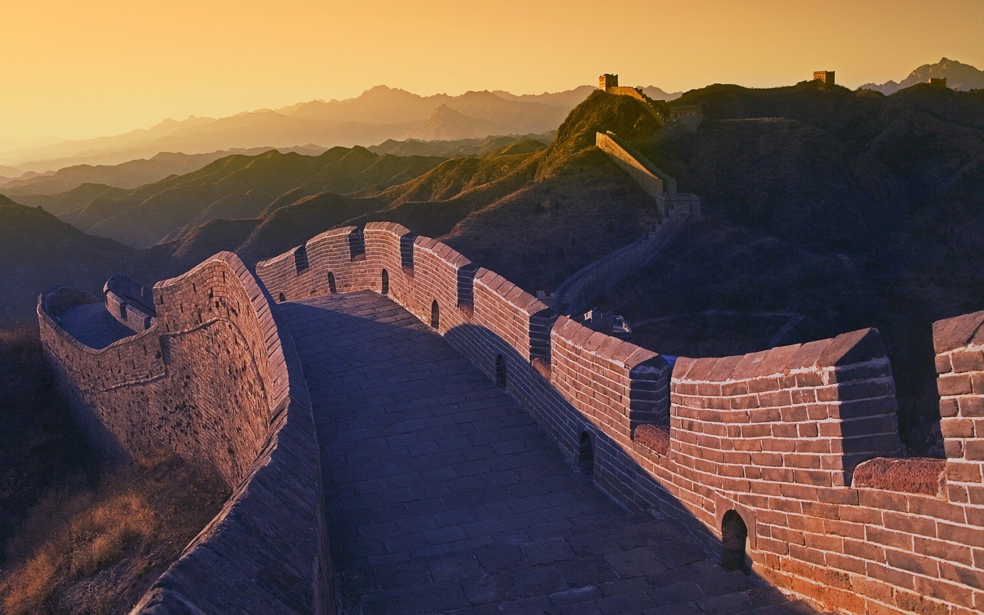 The Great Wall of China, a man-made ancient fortification, stretches across mountainous terrain bathed in warm golden light at sunset.