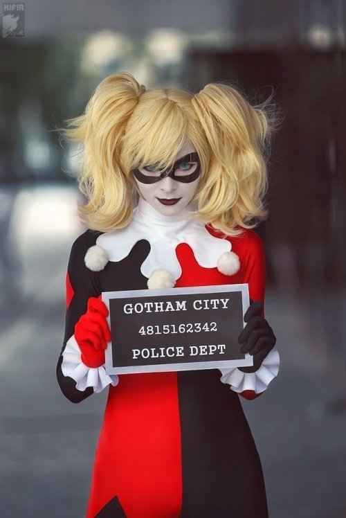 A woman in a vibrant Harley Quinn cosplay holds a sign reading Gotham City Police Dept, featuring a striking black and red costume, complete with playful pigtails.