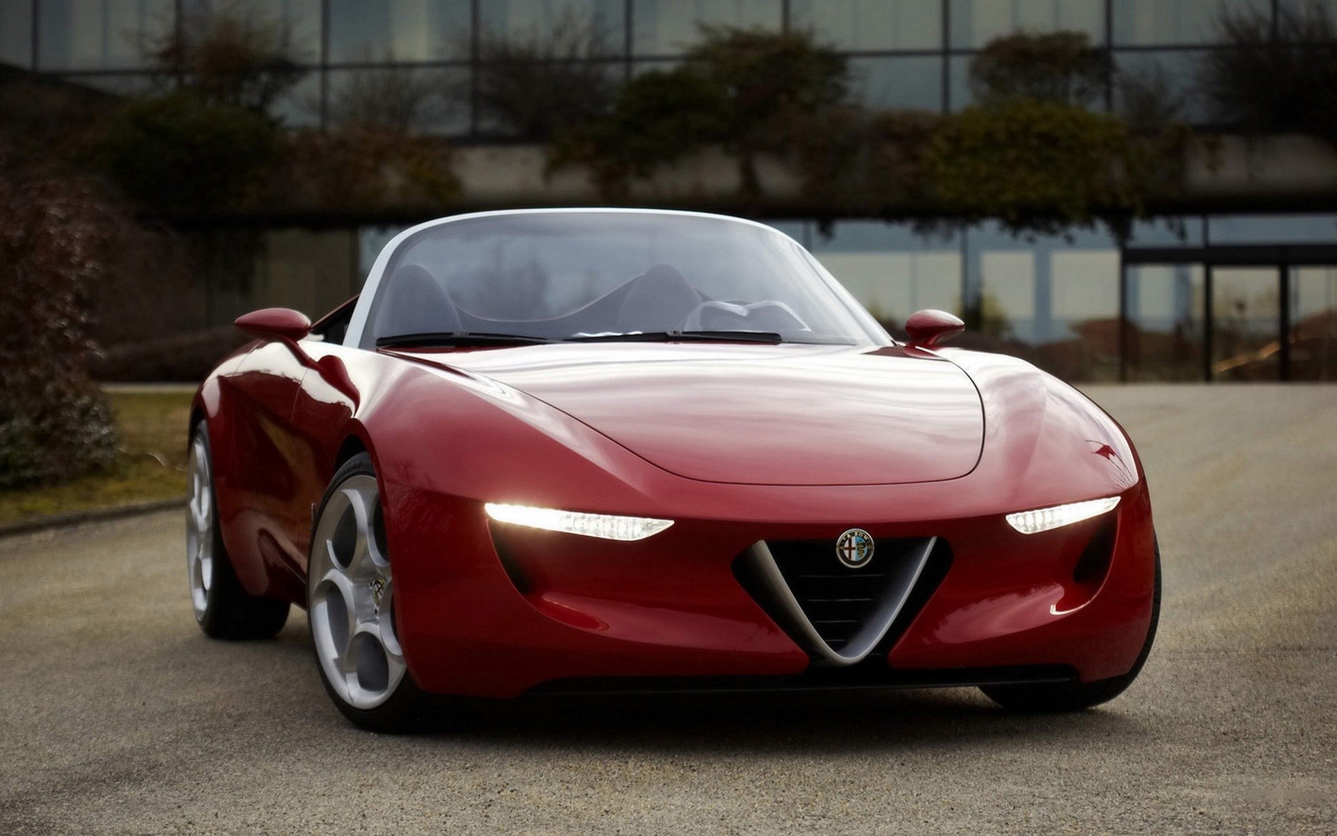 Red Alfa Romeo vehicle — a low-slung sports car with sleek headlights and a signature triangular grille.