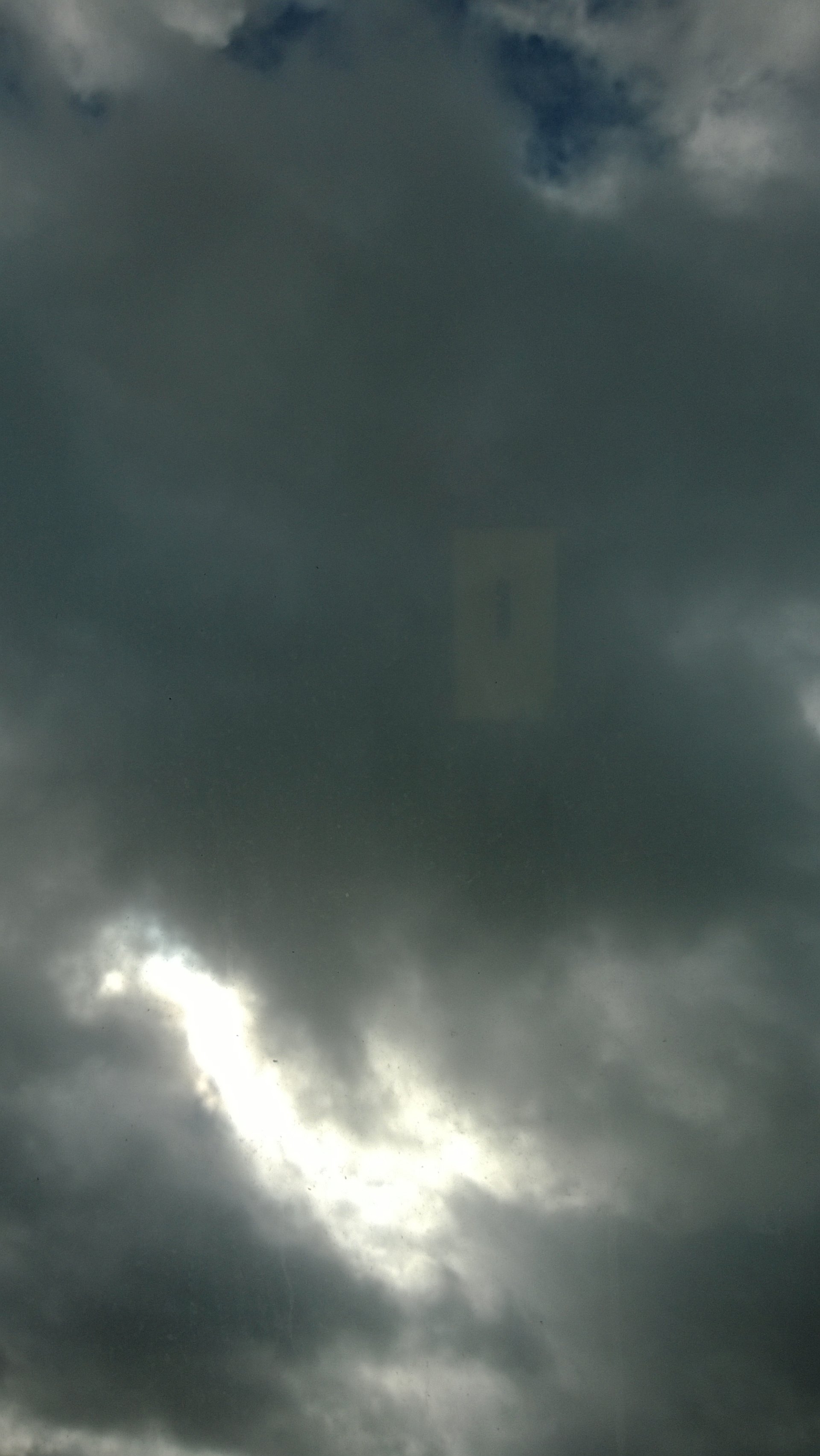 Dark, dense clouds fill the sky with a small break revealing a patch of blue, showcasing a dramatic moment in nature's ever-changing atmosphere.