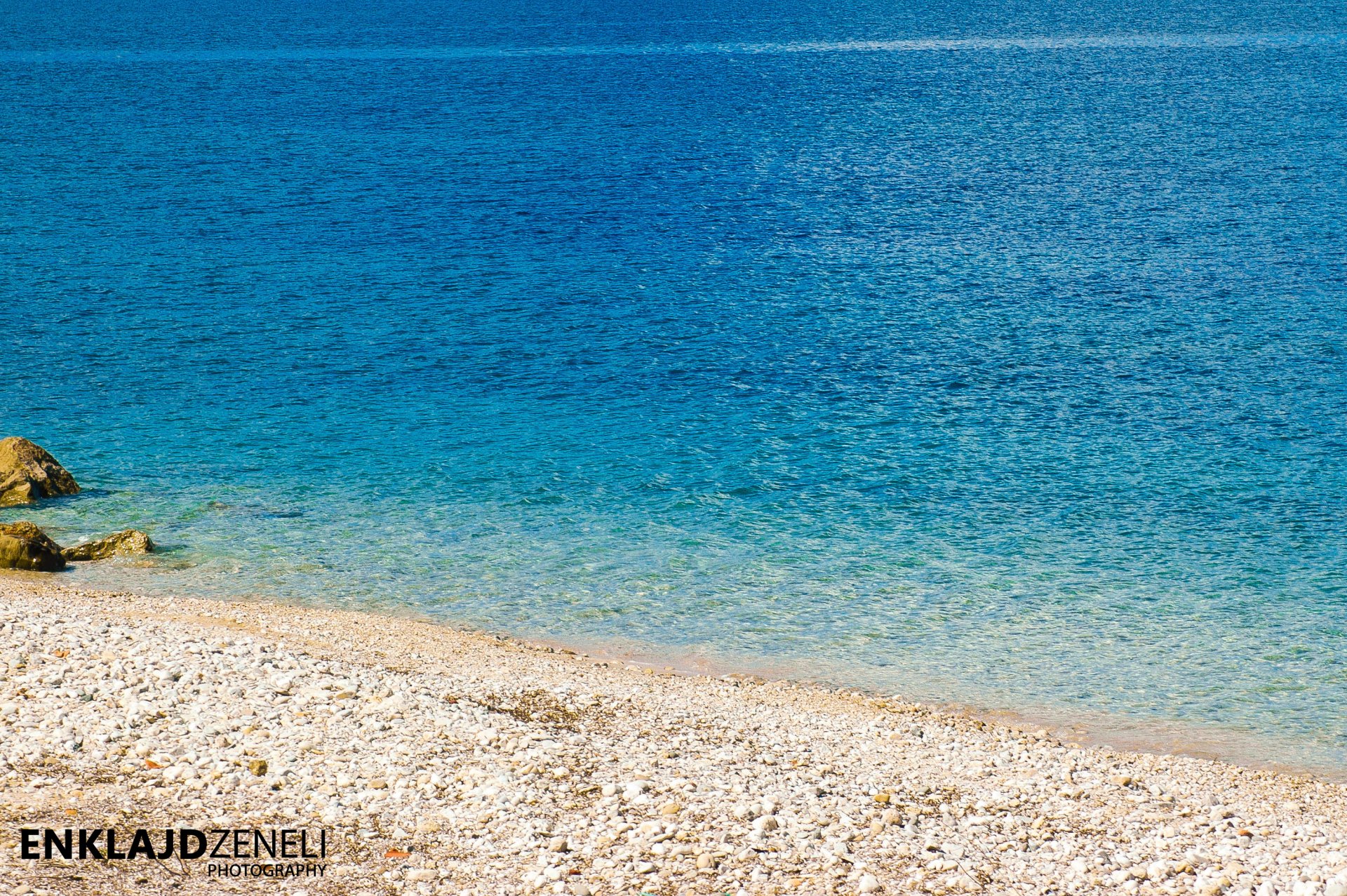 A serene ocean scene showcasing clear blue water meeting a pebble-covered shore, capturing the peaceful essence of nature by the sea.