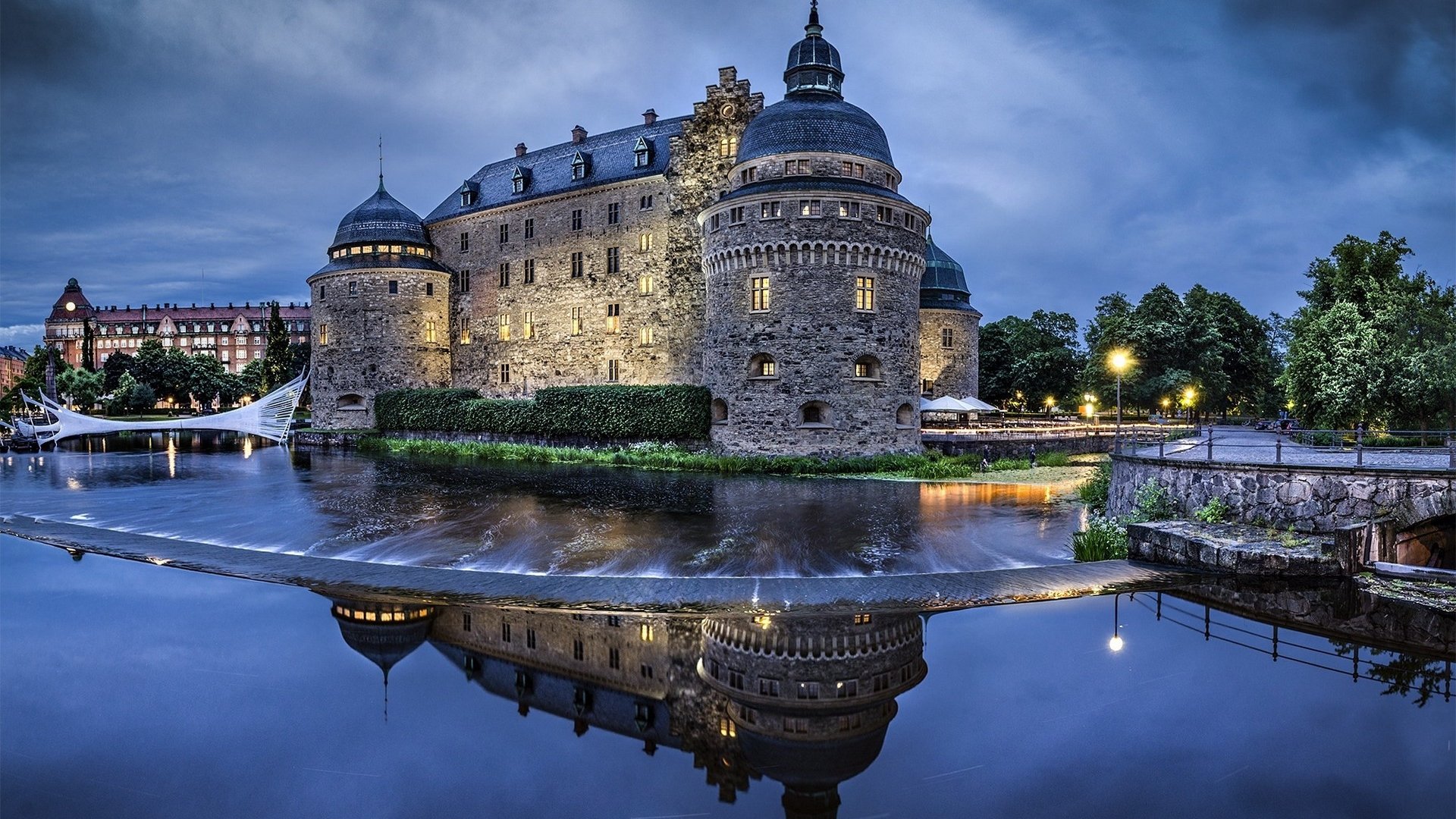 Orebro Castle, a historic man-made fortress, is beautifully illuminated at dusk, reflecting on the calm waters surrounding it.