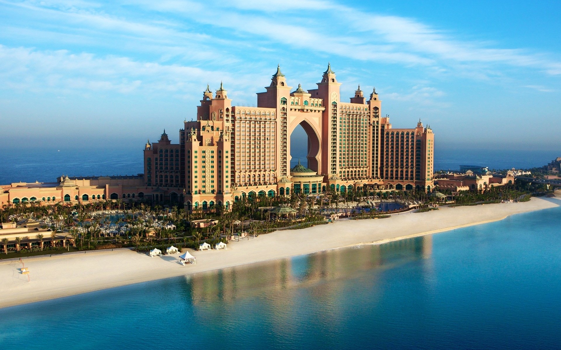Atlantis The Palm, a luxurious man-made resort and hotel in Dubai, sits along a pristine beach with clear blue waters under a bright sky.