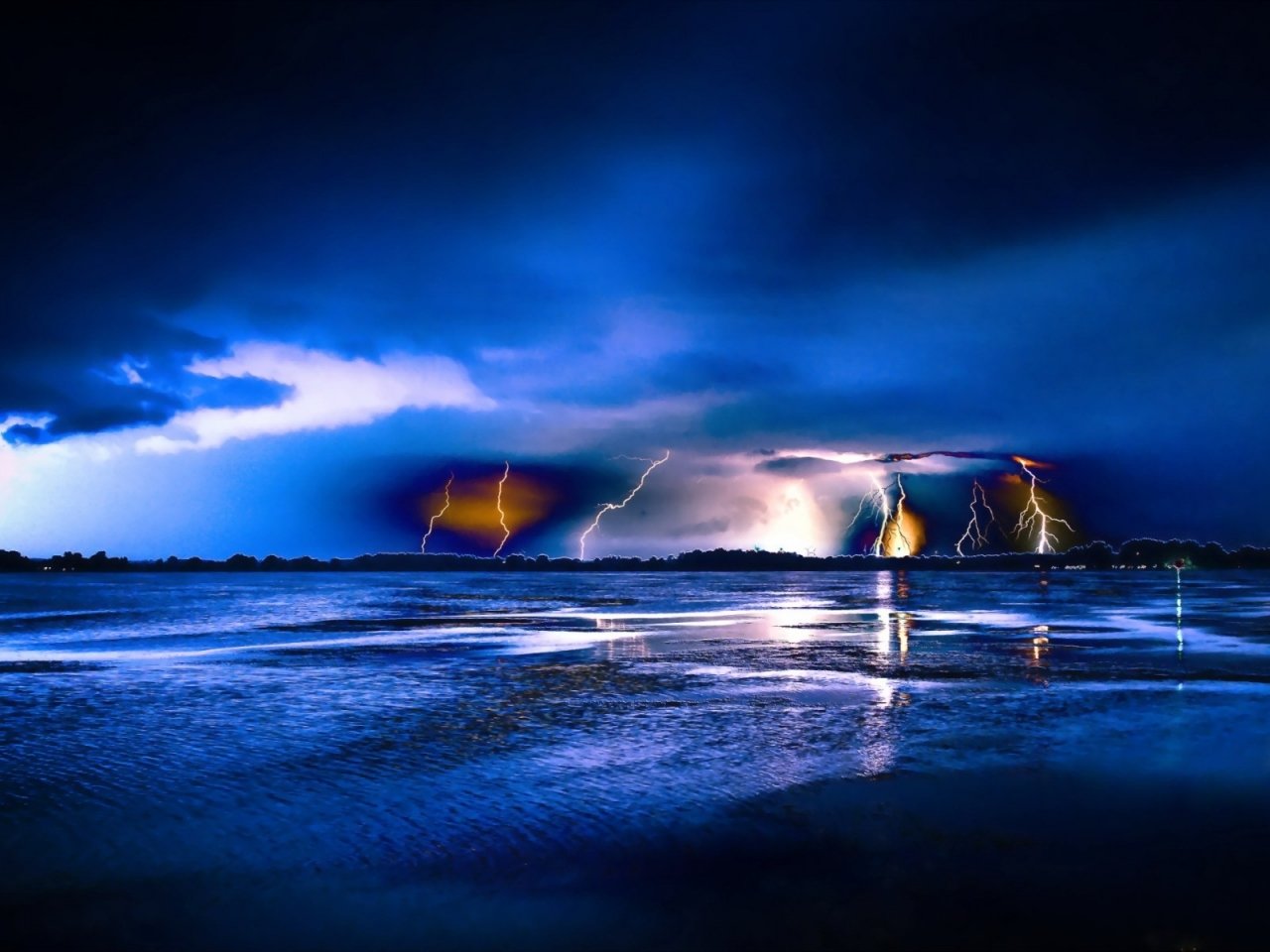 Photography captures multiple lightning bolts striking over a dark, reflective body of water under a stormy, blue-lit sky.