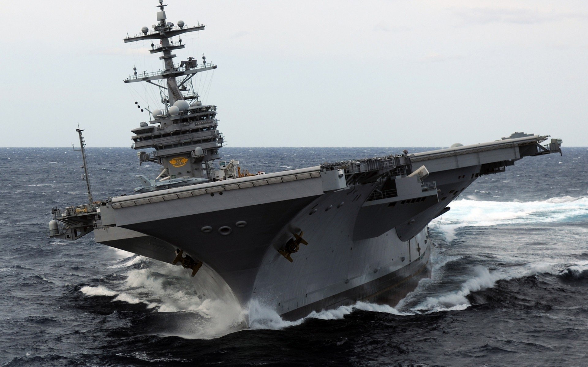 The USS George H.W. Bush (CVN-77), a U.S. Navy aircraft carrier, cuts through the ocean waves under a clear sky.