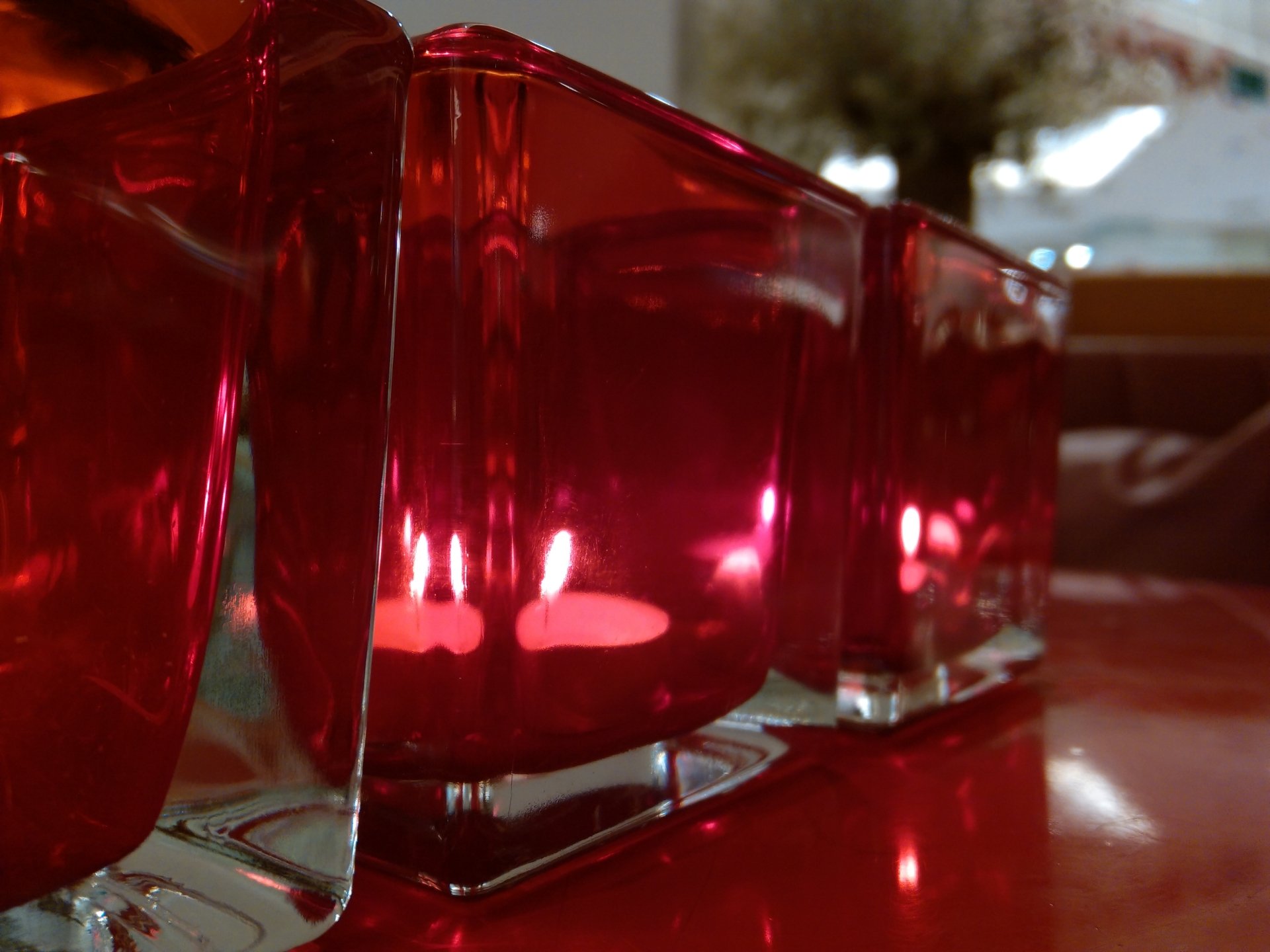 Photography capturing glowing candles inside red glass holders arranged in a row on a reflective surface.