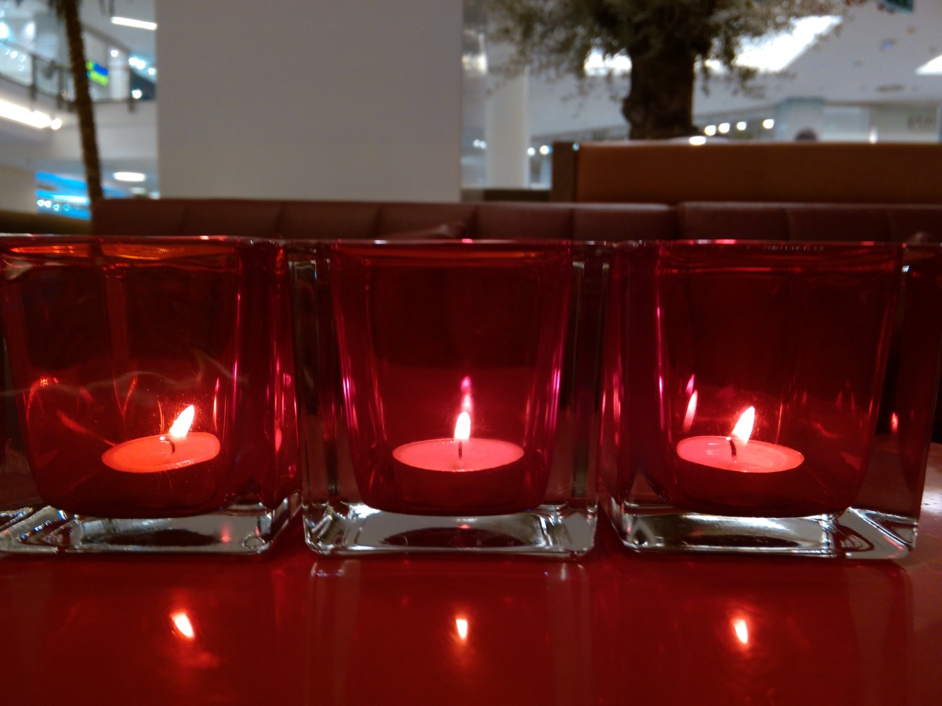 Photography of three red glass votive candle holders with lit tealights casting warm, flickering reflections on a glossy surface.