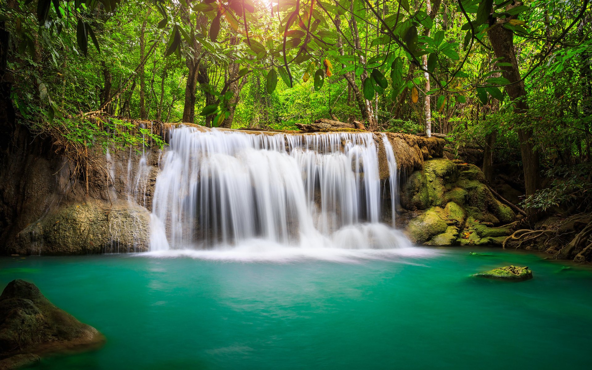 A serene waterfall cascades into a turquoise pool, surrounded by lush greenery and dappled sunlight filtering through the trees, showcasing the beauty of nature.