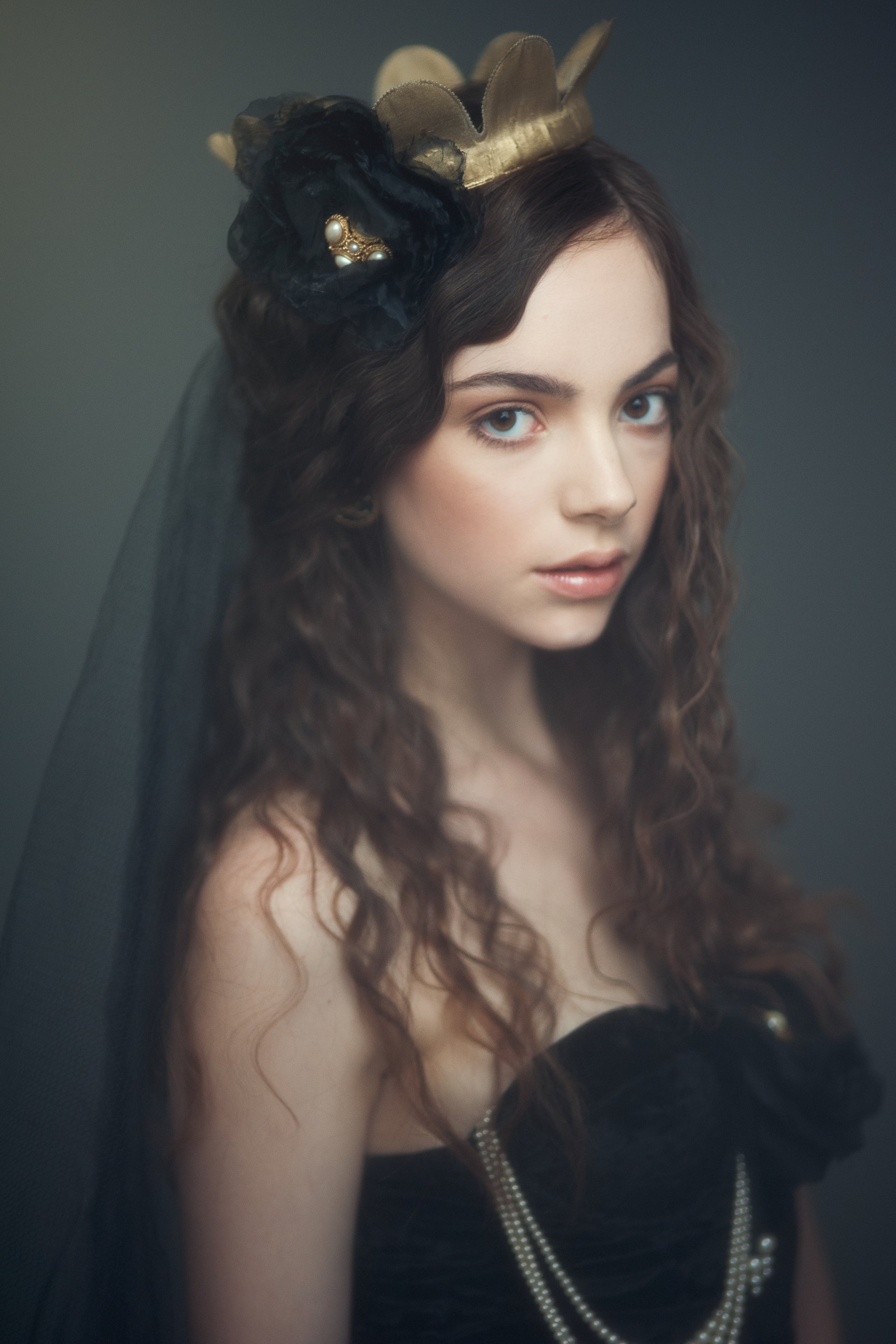 Artistic portrait of Klara Koy, a woman with long curly hair wearing a black dress and a delicate crown, exuding elegance and mystery.