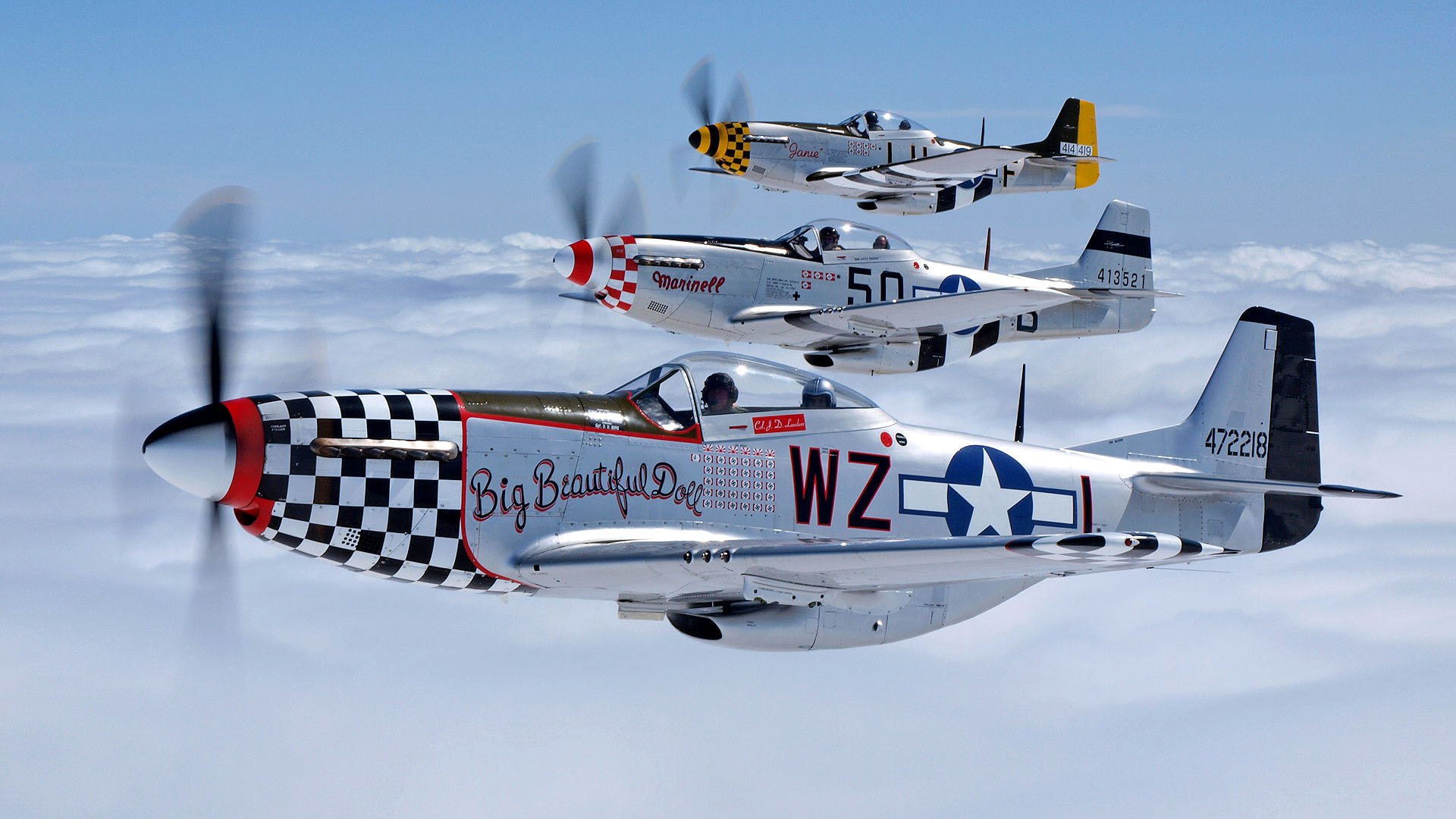 Three North American P-51 Mustang military aircraft fly in formation above the clouds, showcasing distinct nose art and markings on a clear blue day.