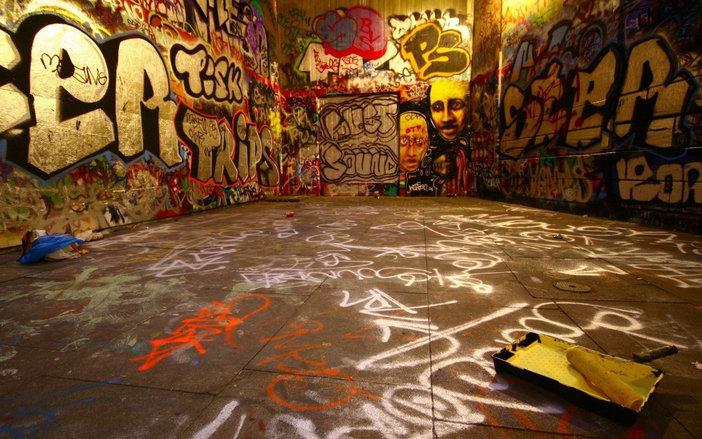 An artistic display of vibrant graffiti fills the walls of a dimly lit room, with scattered paint and tags decorating the floor, showcasing urban creativity and expression.