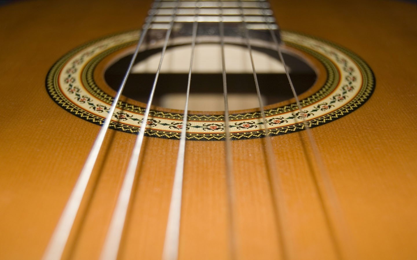Close-up of an acoustic guitar, showcasing its warm wooden surface and detailed rosette around the soundhole, with strings extending towards the viewer.