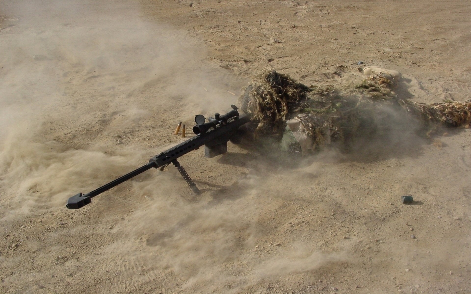 A military sniper's rifle lies on the ground, partially concealed by a camouflage cover, amidst swirling dust in a desert landscape.