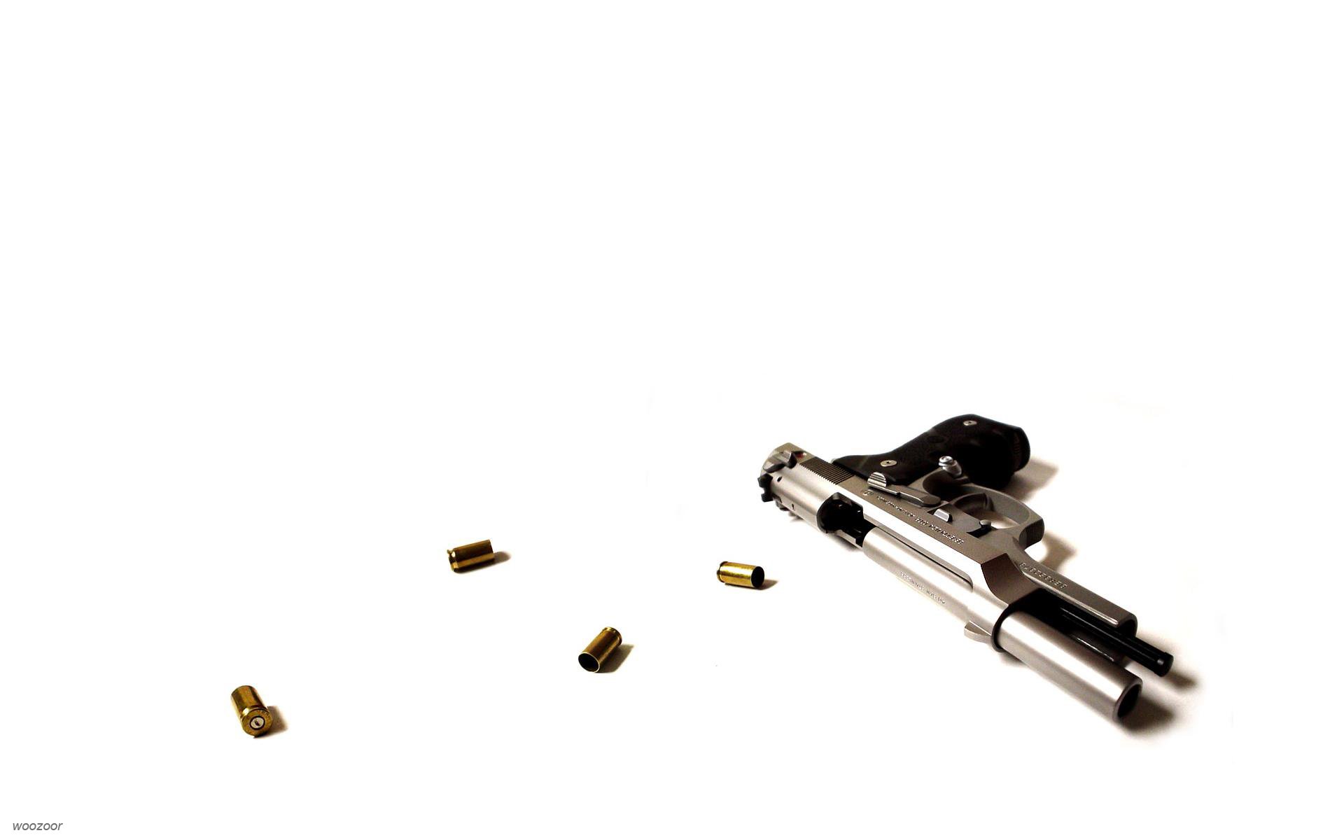 Silver Beretta handgun lying on a white surface with several scattered bullets nearby, showcasing a man-made firearm.