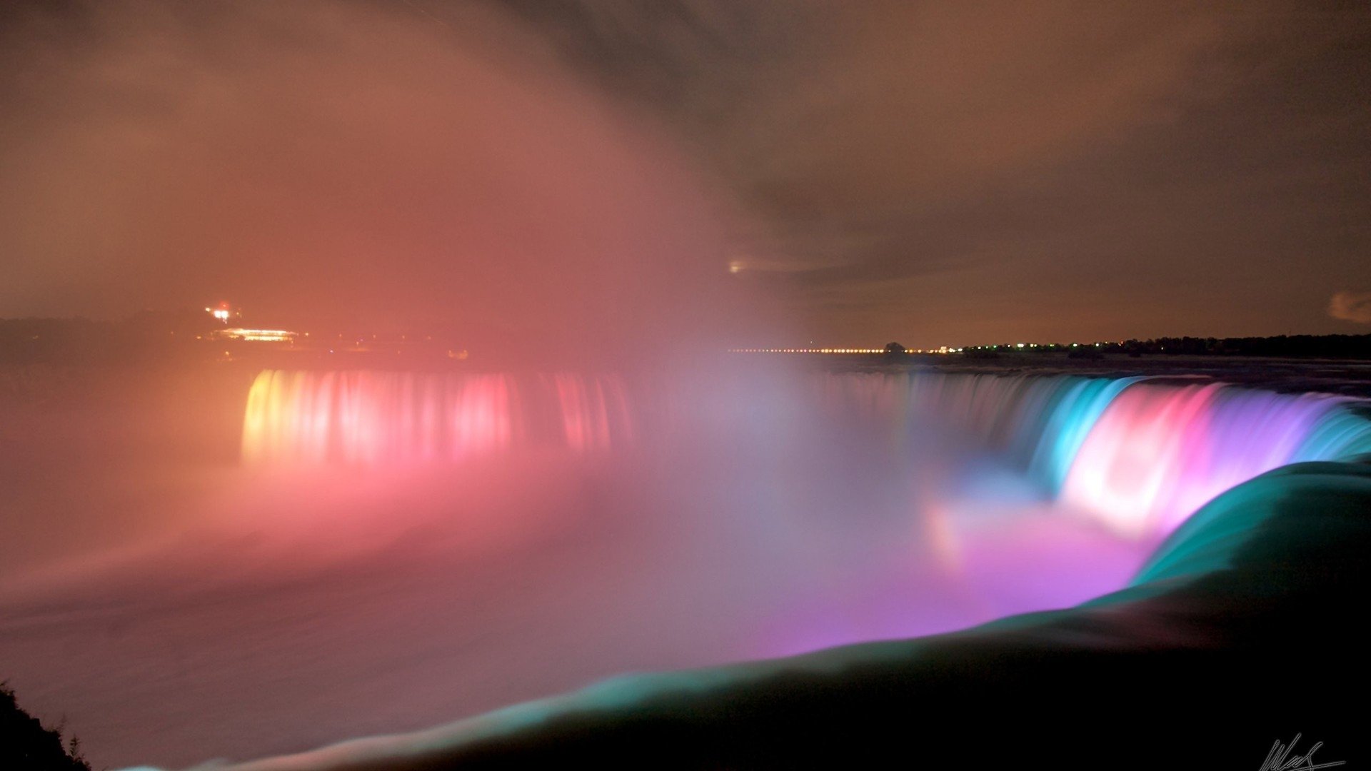A stunning night view of Niagara Falls, illuminated by vibrant colors, with mist rising from the cascading waters, showcasing the beauty of nature in a magical setting.