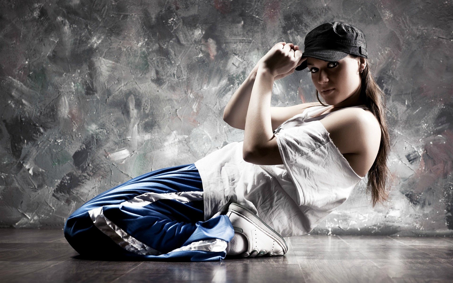 A young woman in casual attire poses on the floor against a textured wall, embodying a dynamic blend of music and dance energy.