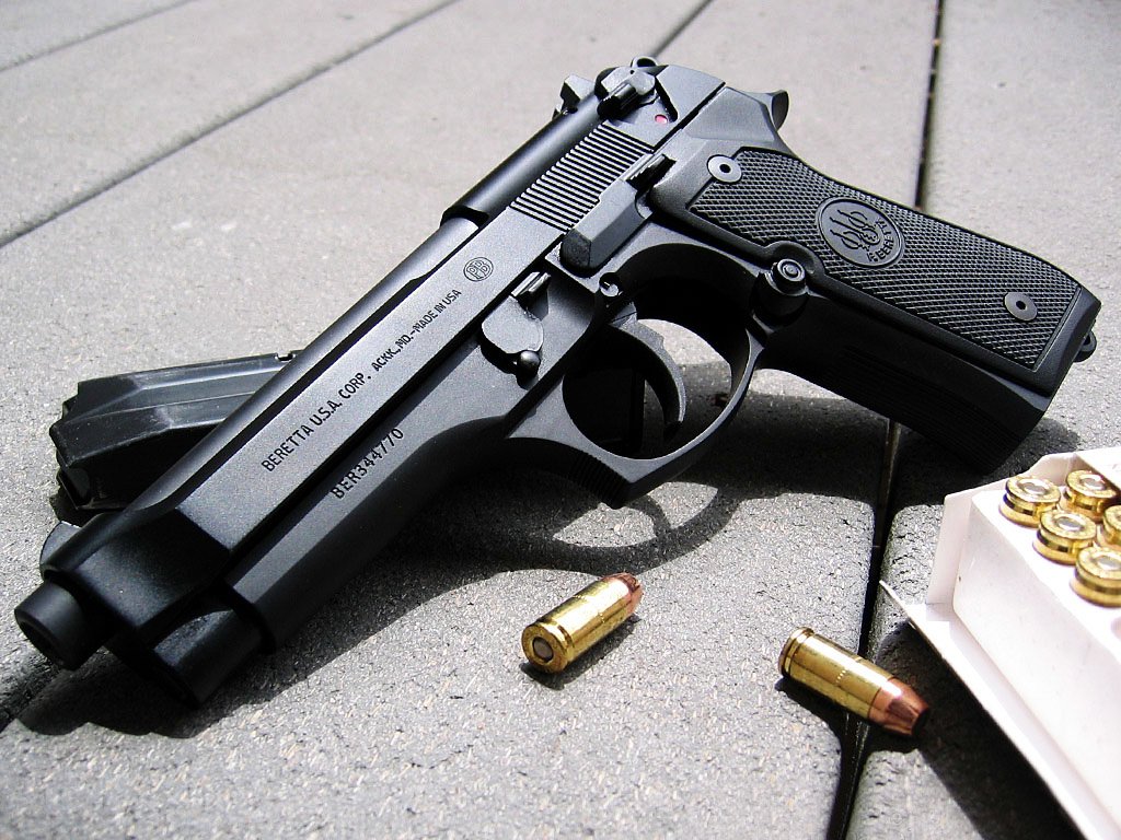 Man-made Beretta semi-automatic pistol with magazine and brass cartridges arranged on a concrete surface.