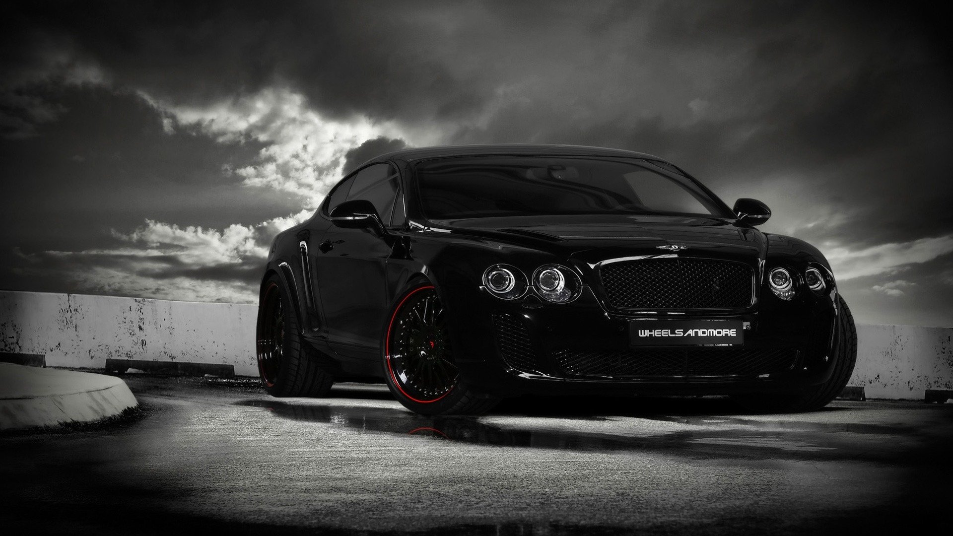 Low-angle view of a black Bentley Continental GT with red-accent wheels parked on concrete under dramatic storm clouds, glossy finish reflecting moody lighting.
