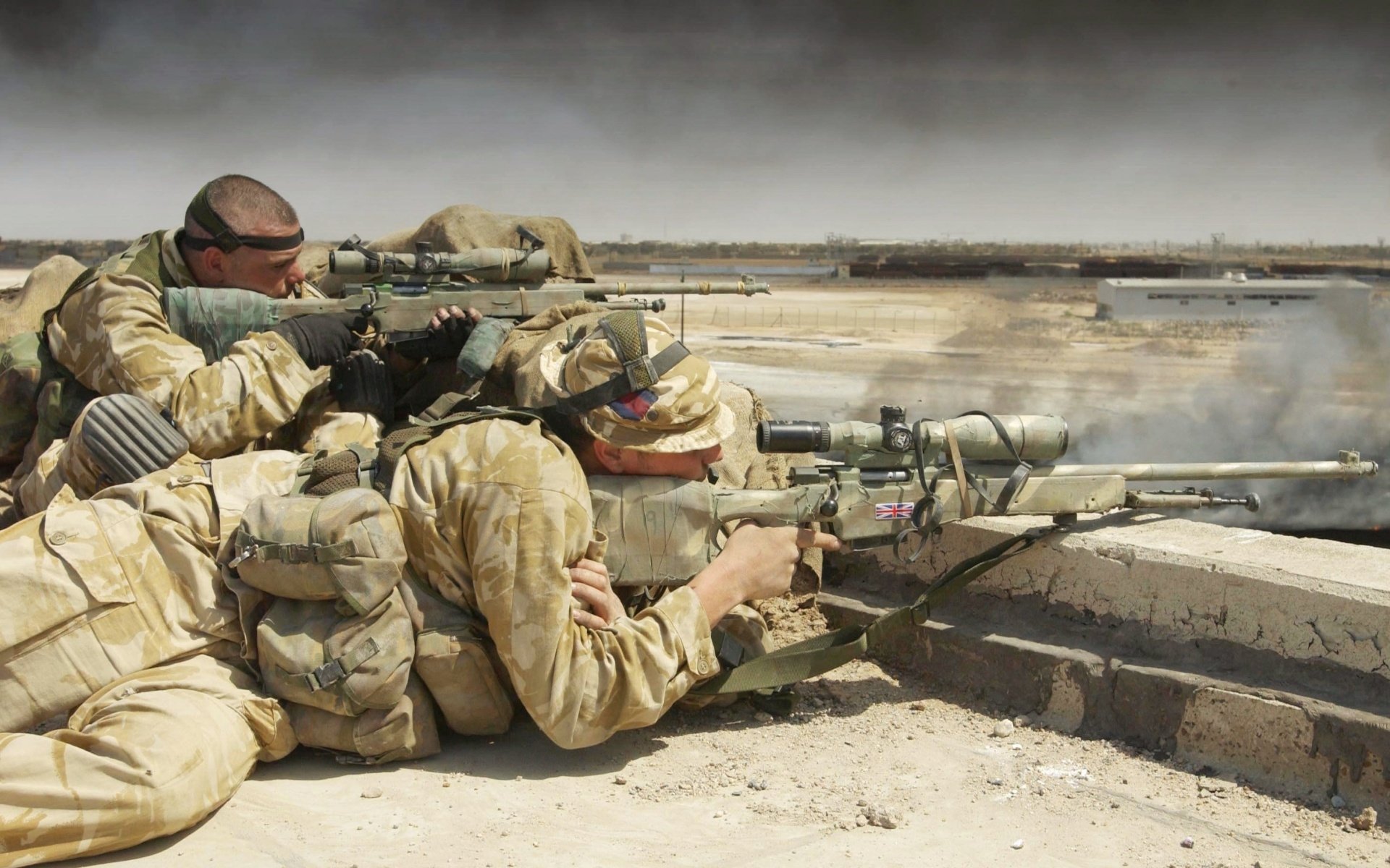 Two soldiers in military gear are aiming their sniper rifles from a high vantage point, focused on a distant target in a war-torn landscape.