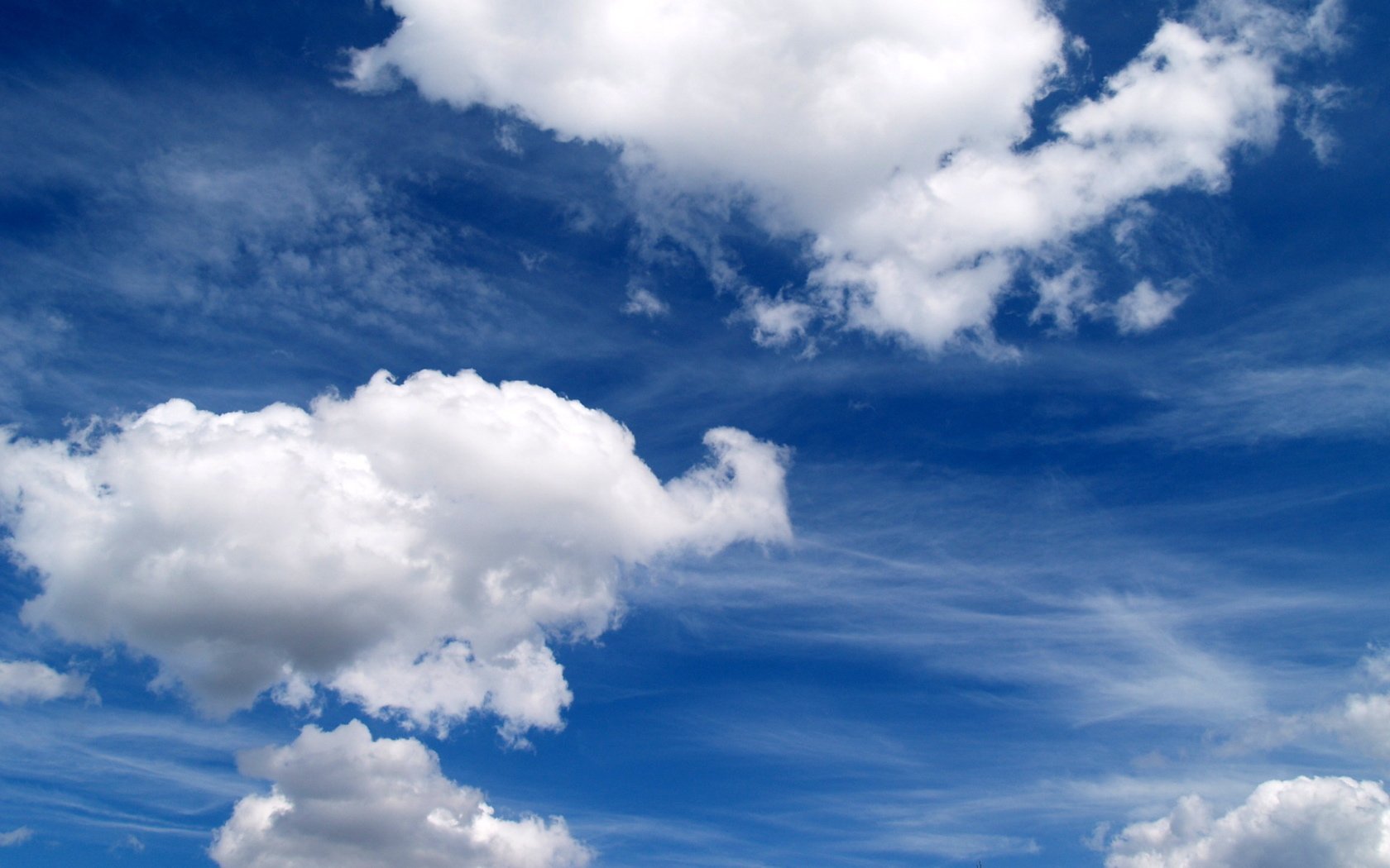 Nature scene: a deep blue sky streaked with wispy cirrus clouds and dotted with fluffy cumulus clouds.