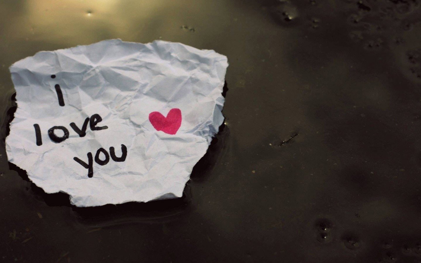 A crumpled note reading I love you with a heart symbol, resting on a dark surface, evokes a sense of artistic expression and deep emotion.