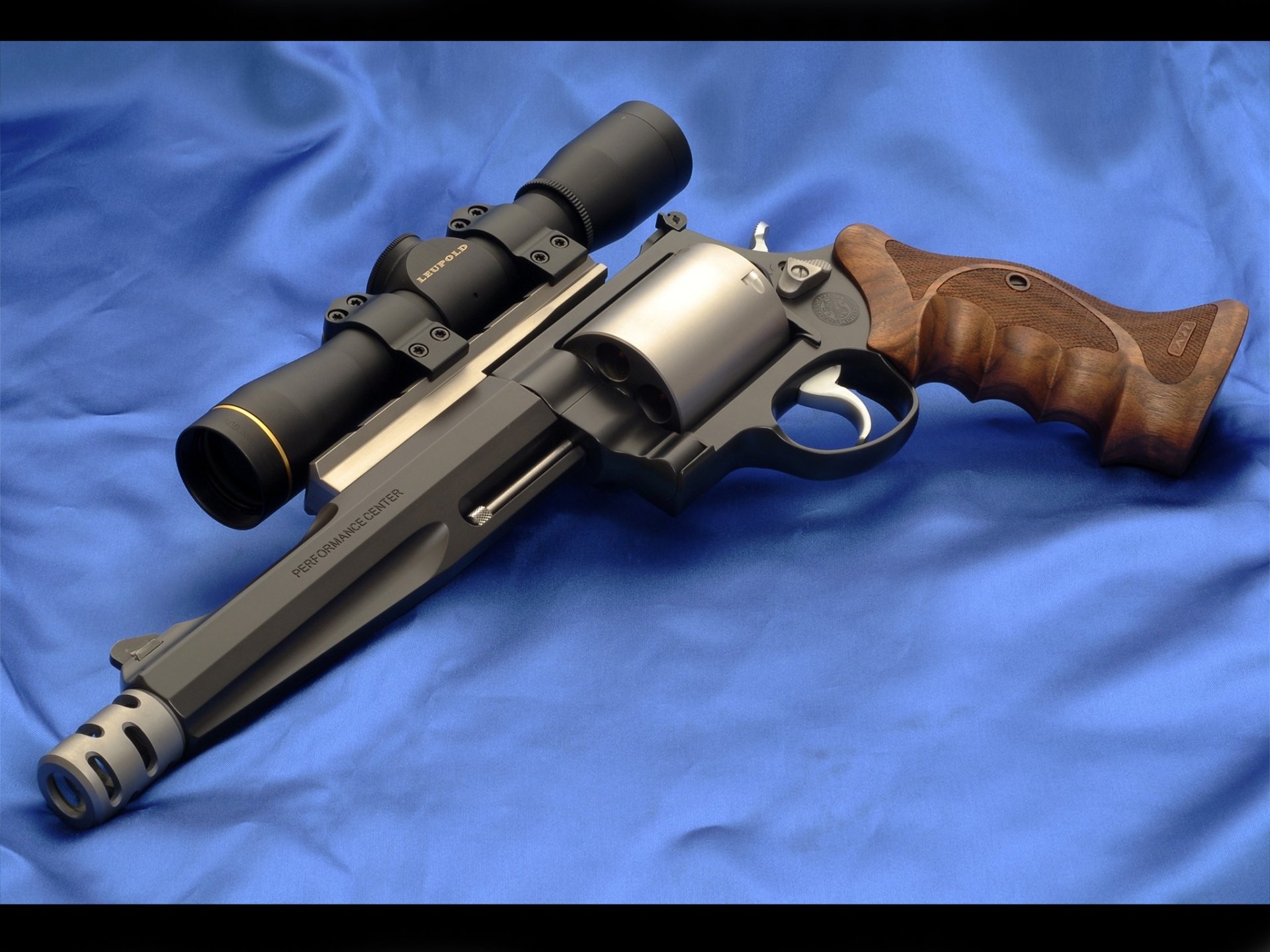 A Smith & Wesson revolver with a wooden grip and mounted scope, displayed on a blue fabric background.