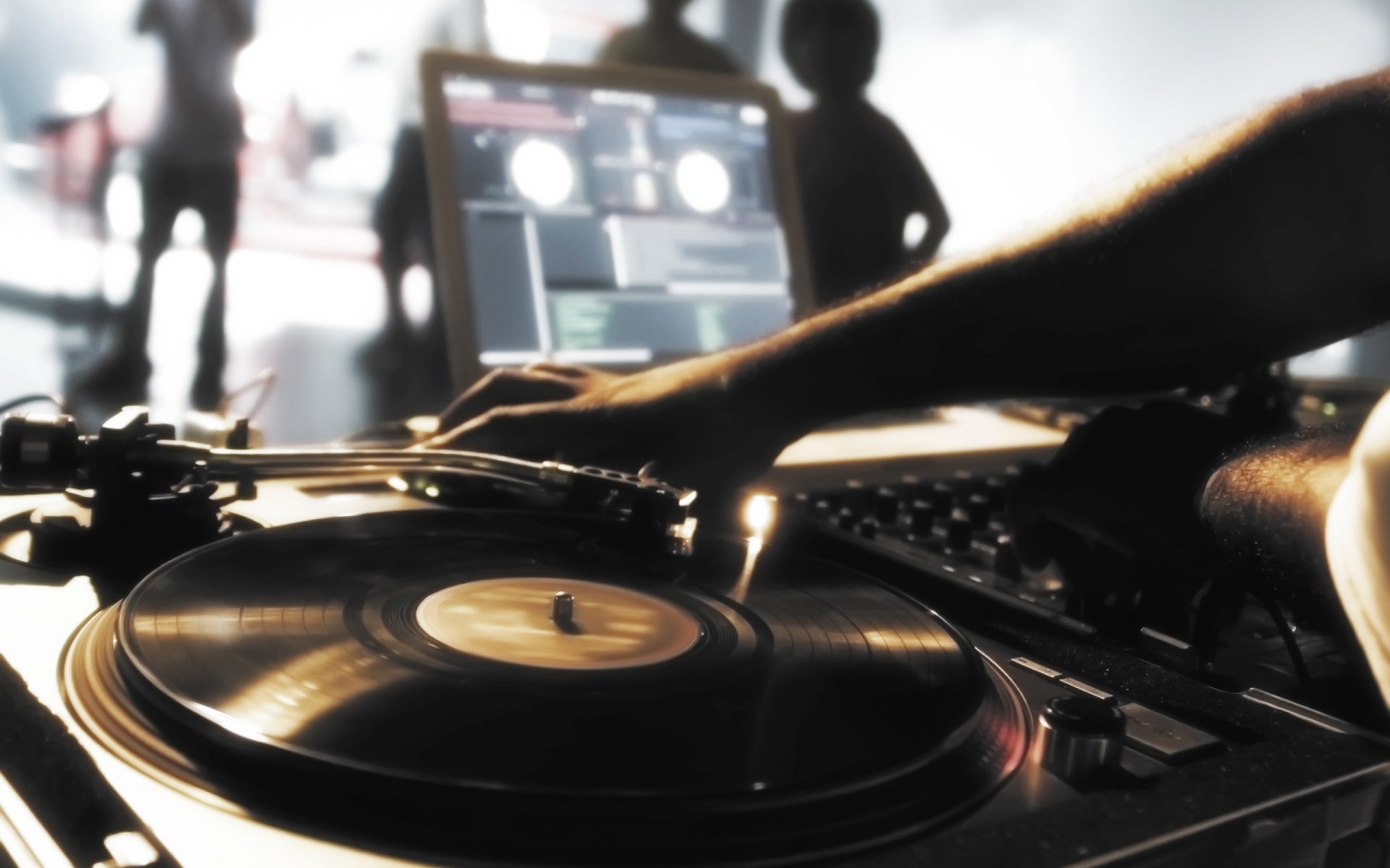 Close-up of a DJ manipulating a vinyl turntable with laptop and silhouetted crowd in background, live music atmosphere.