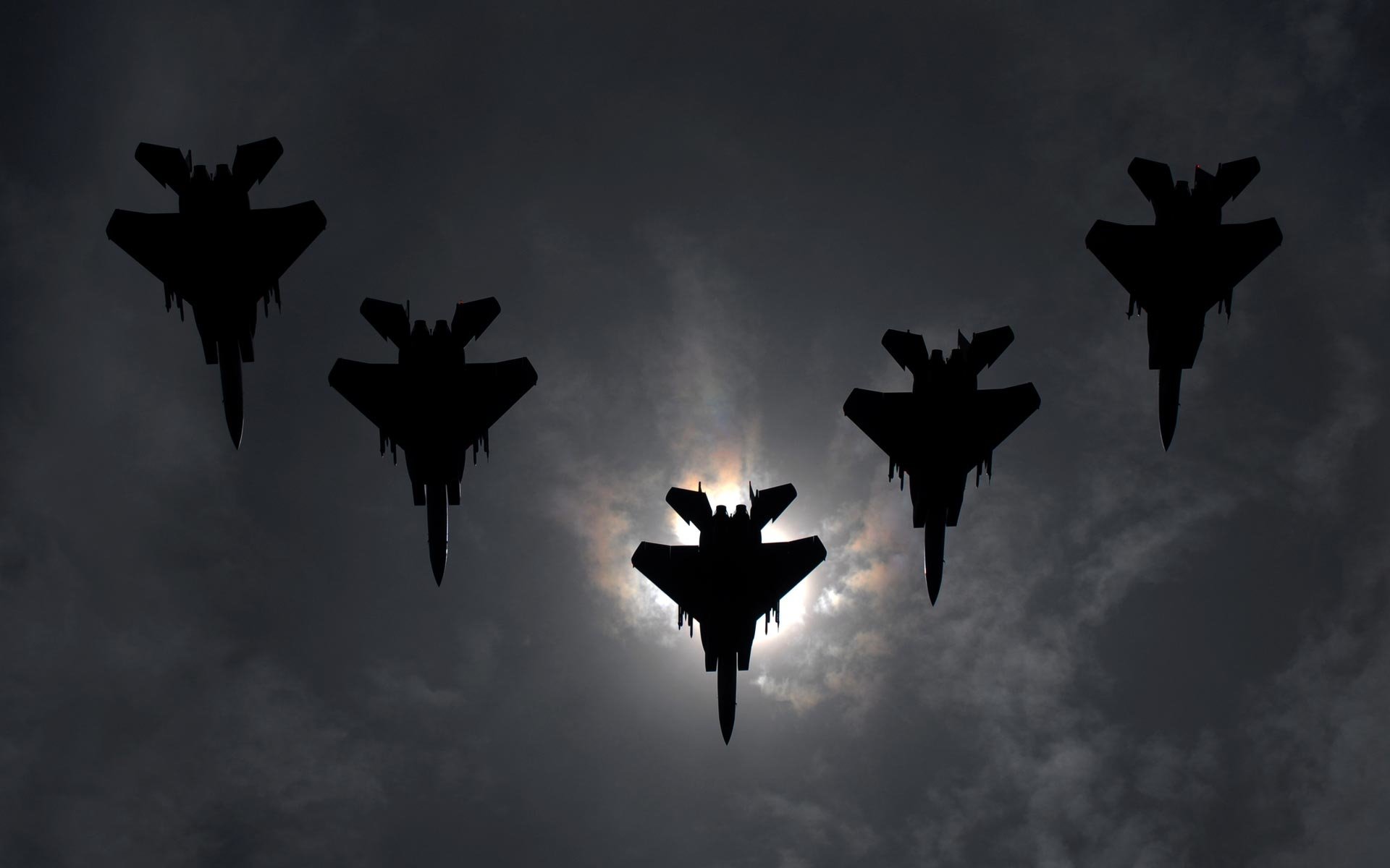 Five military jet fighters soar against a dramatic sky, silhouetted by the sun, showcasing their imposing presence and power.