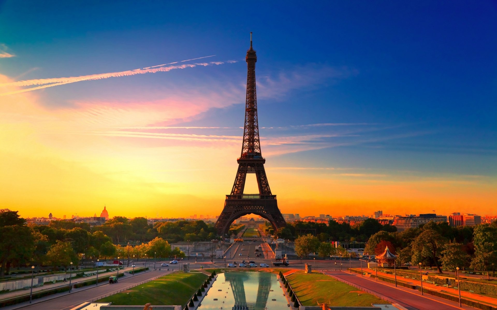 A stunning view of the Eiffel Tower at sunset, surrounded by lush greenery and a tranquil pool, showcasing the beauty of this iconic man-made structure in Paris.