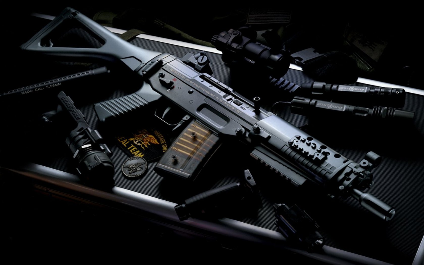 A close-up image of a man-made assault rifle, featuring various tactical attachments, set against a dark background with military-related items nearby.