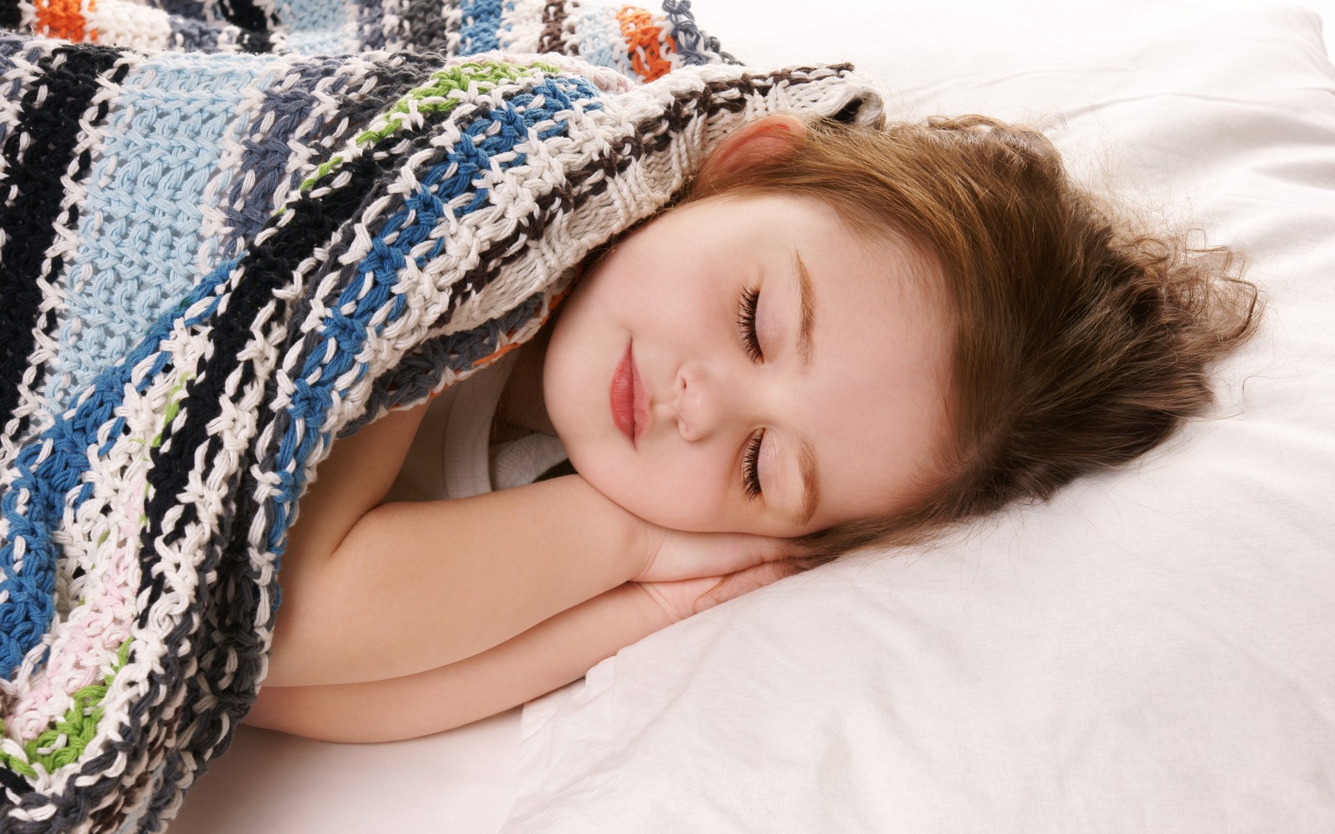 A child sleeping peacefully under a colorful blanket, with a serene expression, creating a warm and cozy atmosphere in the photography.