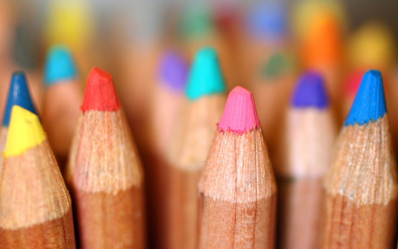 A close-up photograph of colorful pencil tips, showcasing vibrant shades like red, blue, and green, arranged in a dynamic composition.