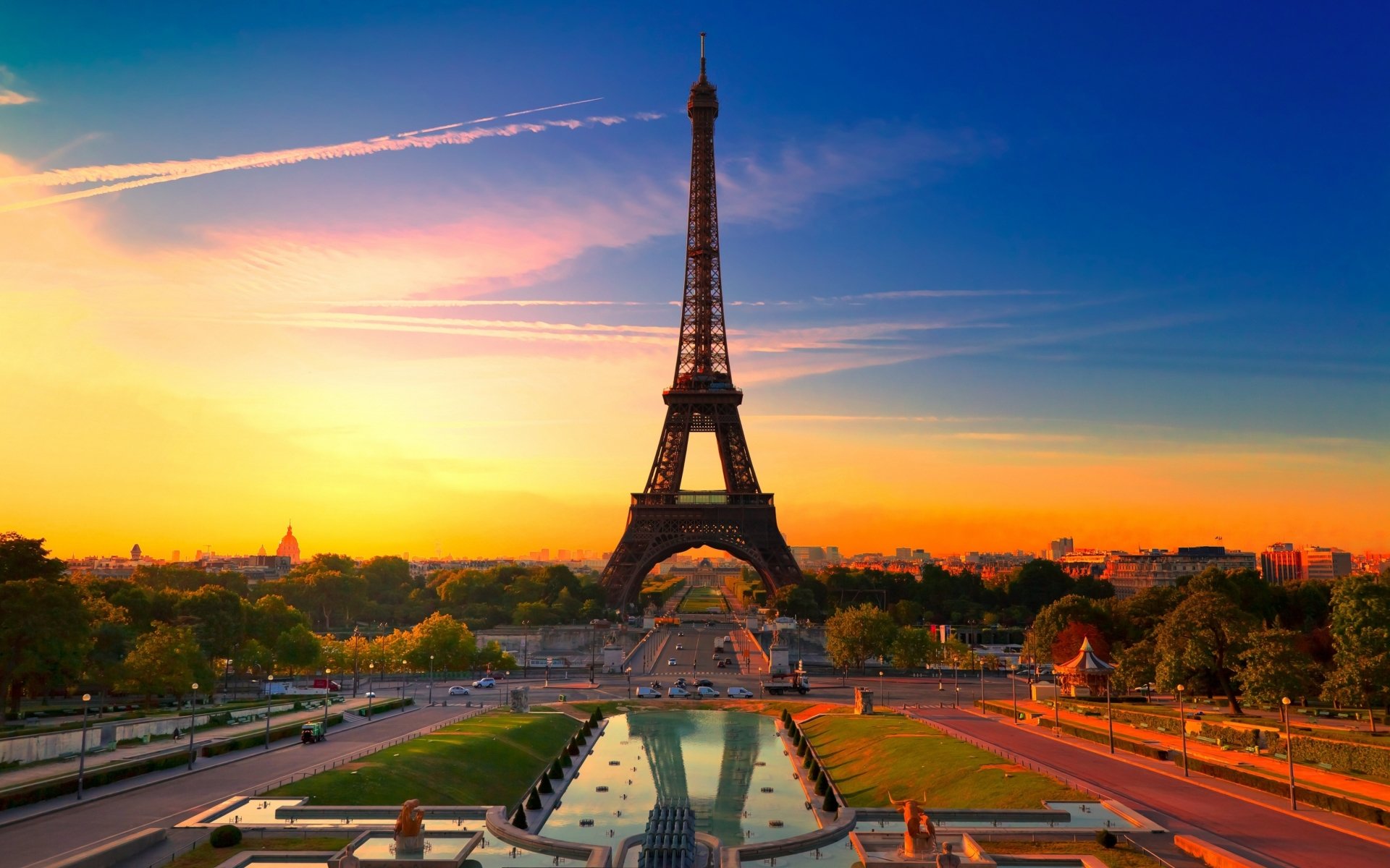 A stunning view of the Eiffel Tower at sunset, surrounded by greenery and a fountain, showcasing the iconic man-made structure against a vibrant sky.