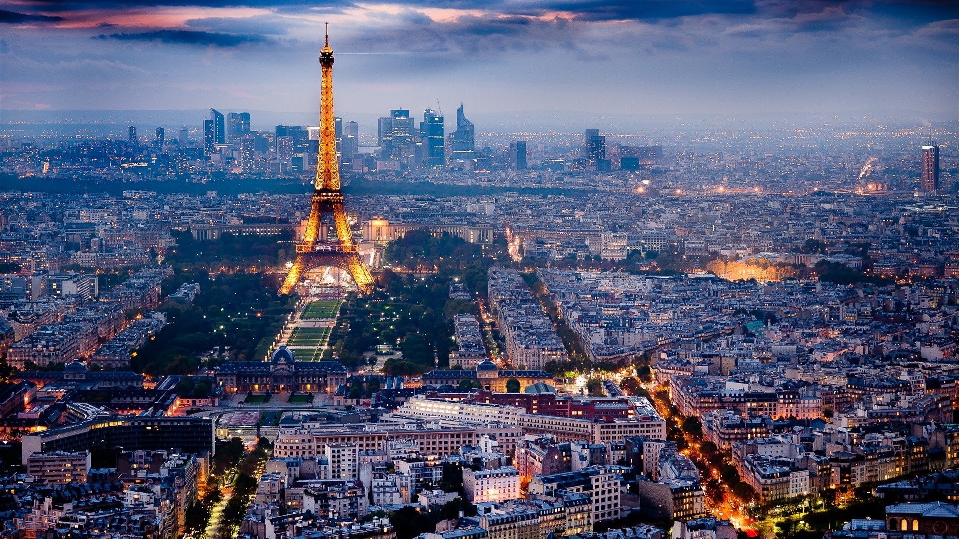 A stunning aerial view of Paris at dusk, featuring the illuminated Eiffel Tower standing tall among the city's skyline and intricate man-made architecture.