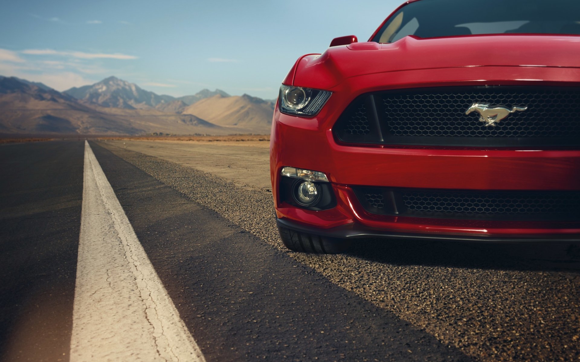 Red Ford Mustang vehicle parked on a deserted road with desert mountains in the background under a clear sky.