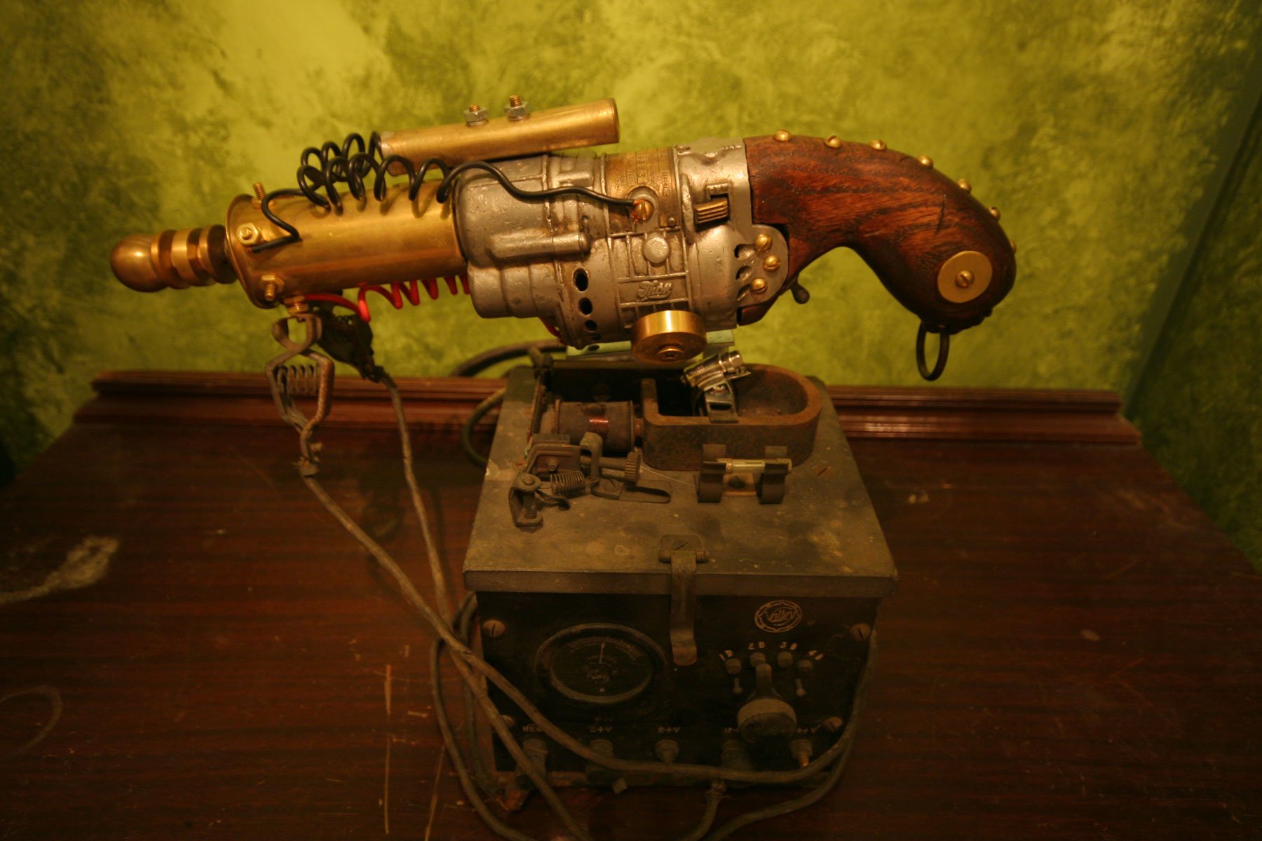 A detailed sci-fi weapon with metallic and wooden components, resting on a vintage control box against a green backdrop.