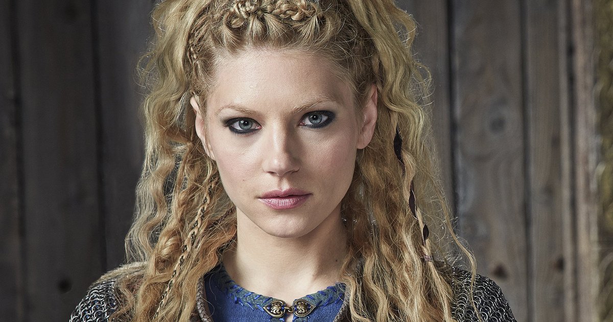 Portrait of a determined woman with long braided blonde hair from the TV show Vikings (2013), set against a rustic wooden background.