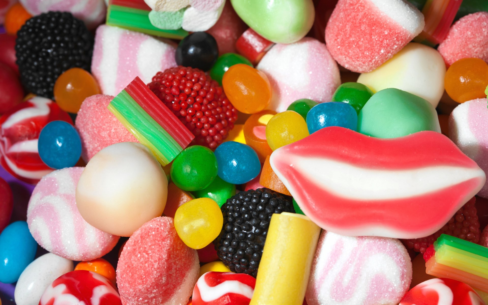 A vibrant assortment of colorful candies, including gummy lips, jellybeans, and striped sweets, creates a playful and inviting display of tempting treats.