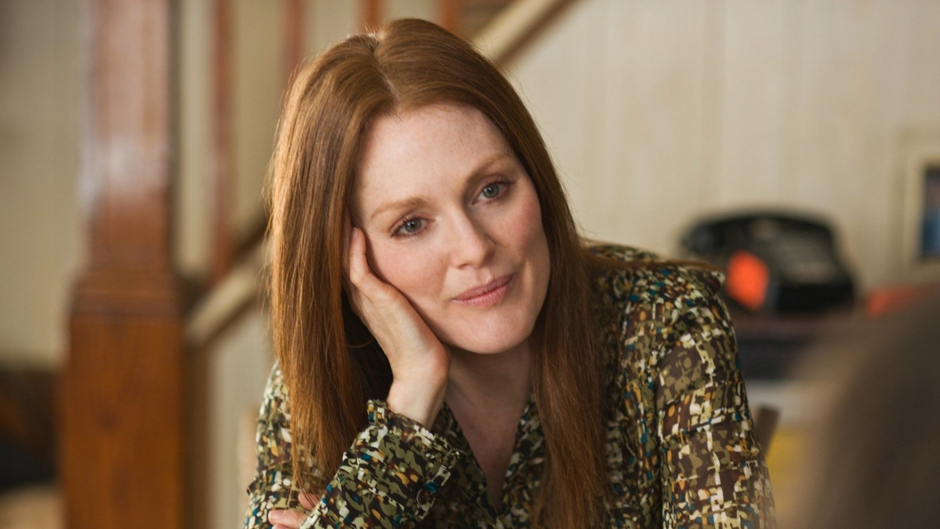 Scene from the movie Being Flynn showing a woman with long red hair resting her head on her hand, looking thoughtfully ahead in a softly lit room.
