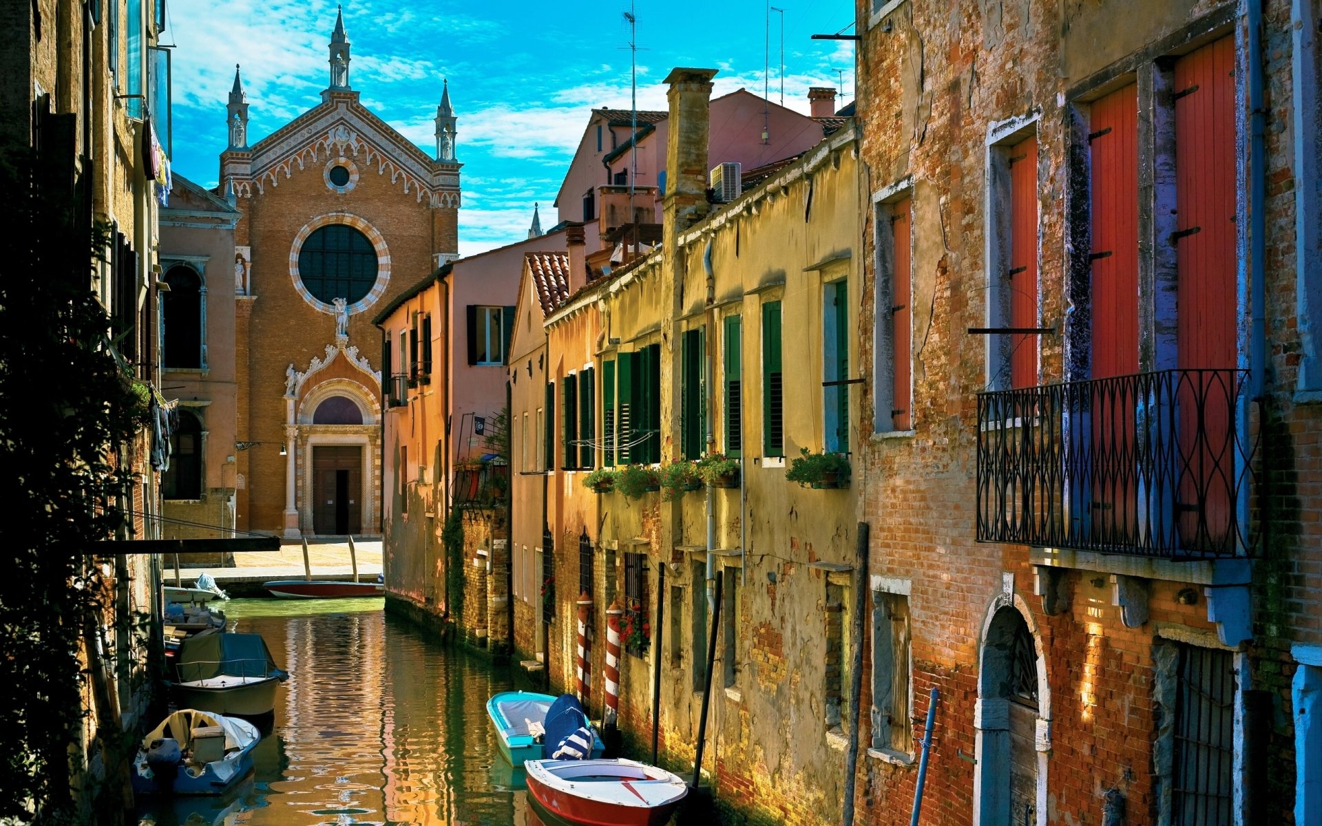 A picturesque view of a canal in Venice, featuring colorful buildings, boats, and a historic church in the background, showcasing the city's unique man-made charm.