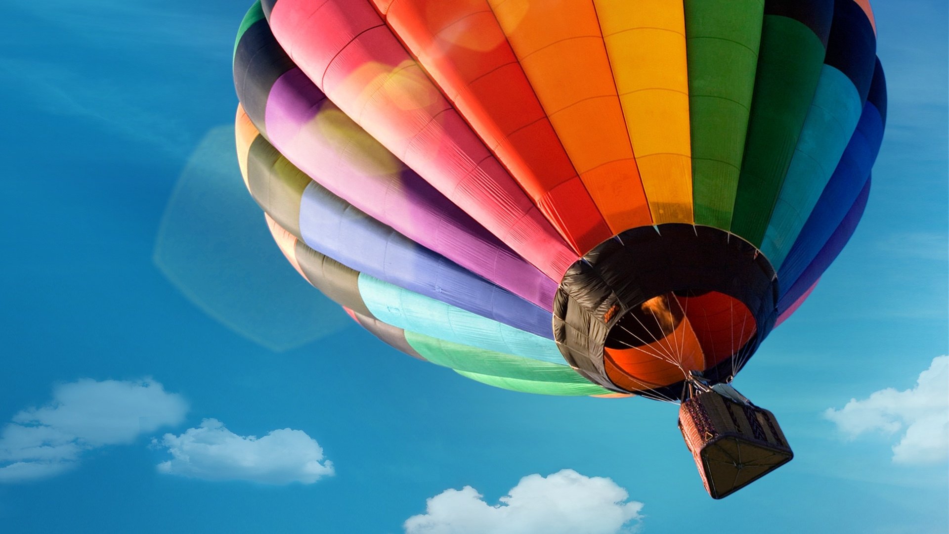A vibrant hot air balloon with a rainbow pattern floats gently against a clear blue sky, showcasing its colorful design and unique vehicle form.